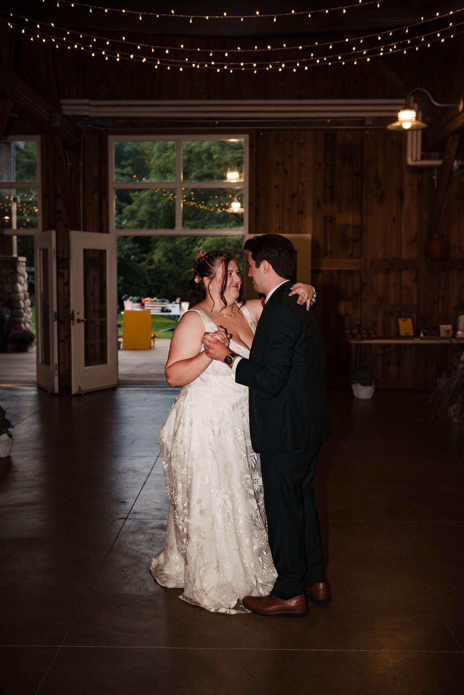 Romantic first dance under twinkling string lights in a rustic barn reception venue.