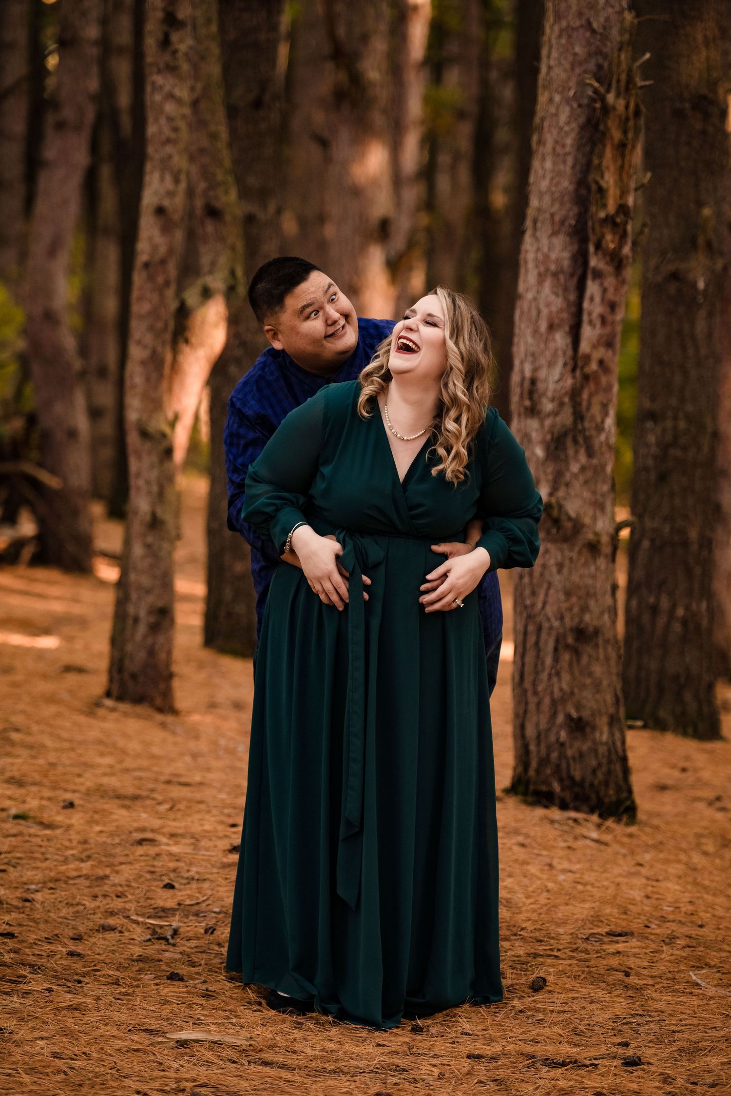 Two people in dark formal wear share a joyful moment in a pine forest.