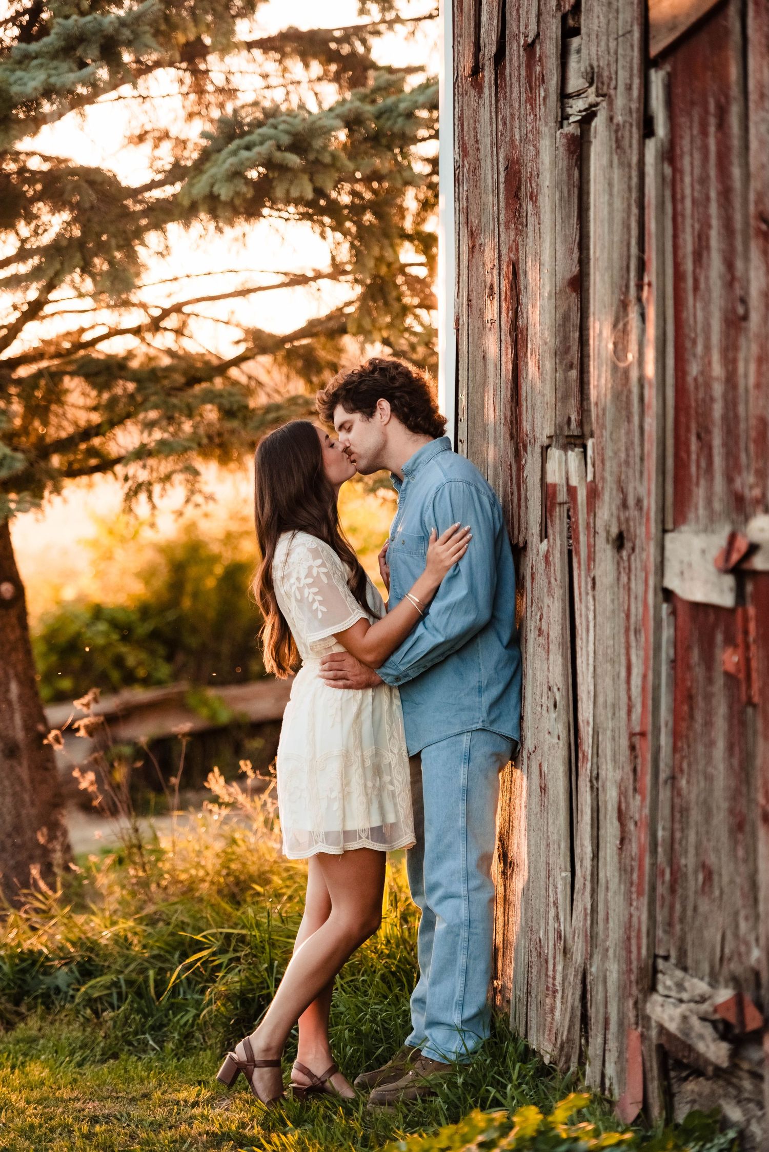 Romantic couple embraces against rustic wooden barn wall at sunset in golden light.