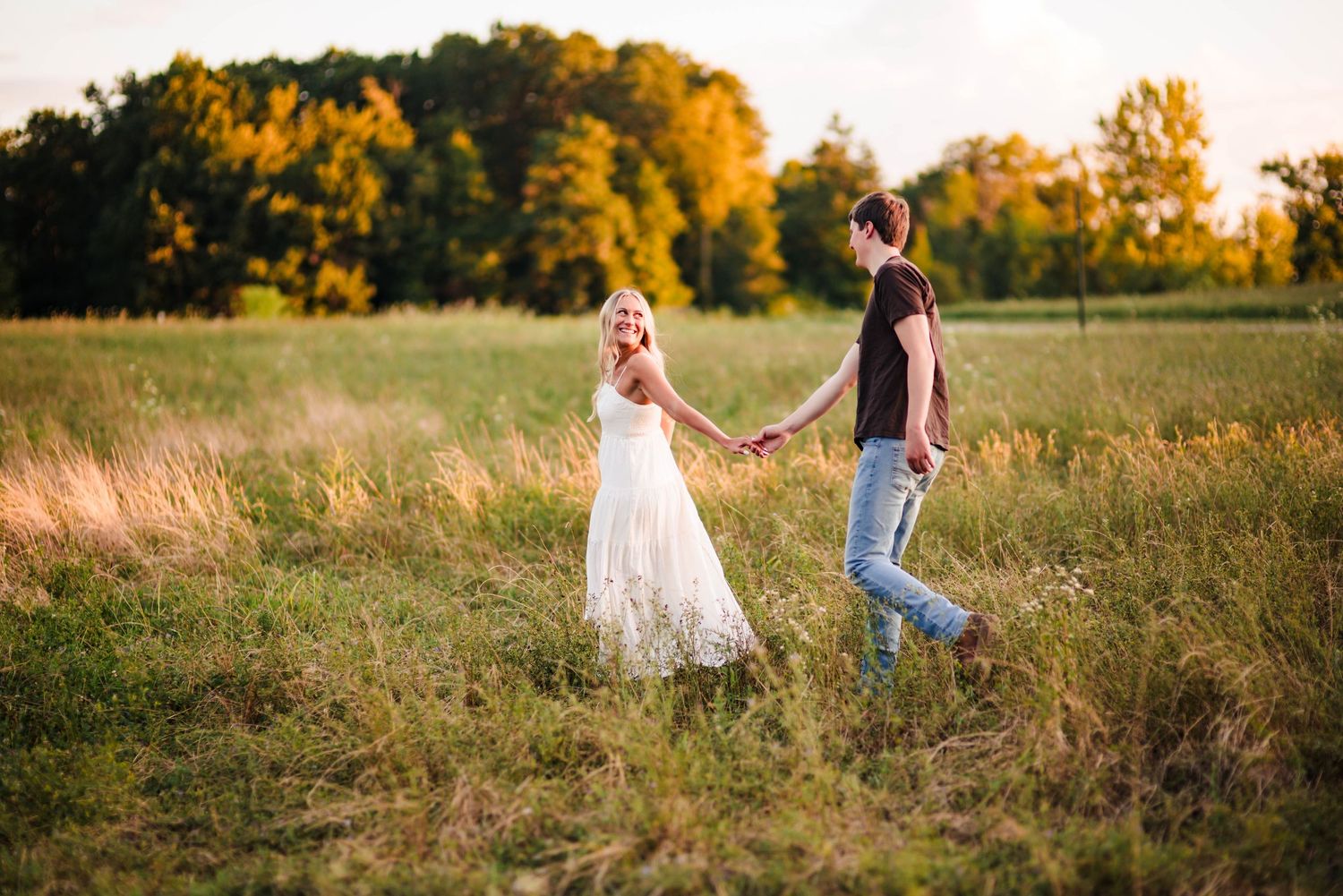 Couple walking through a golden autumn field at sunset with flowing white dress.