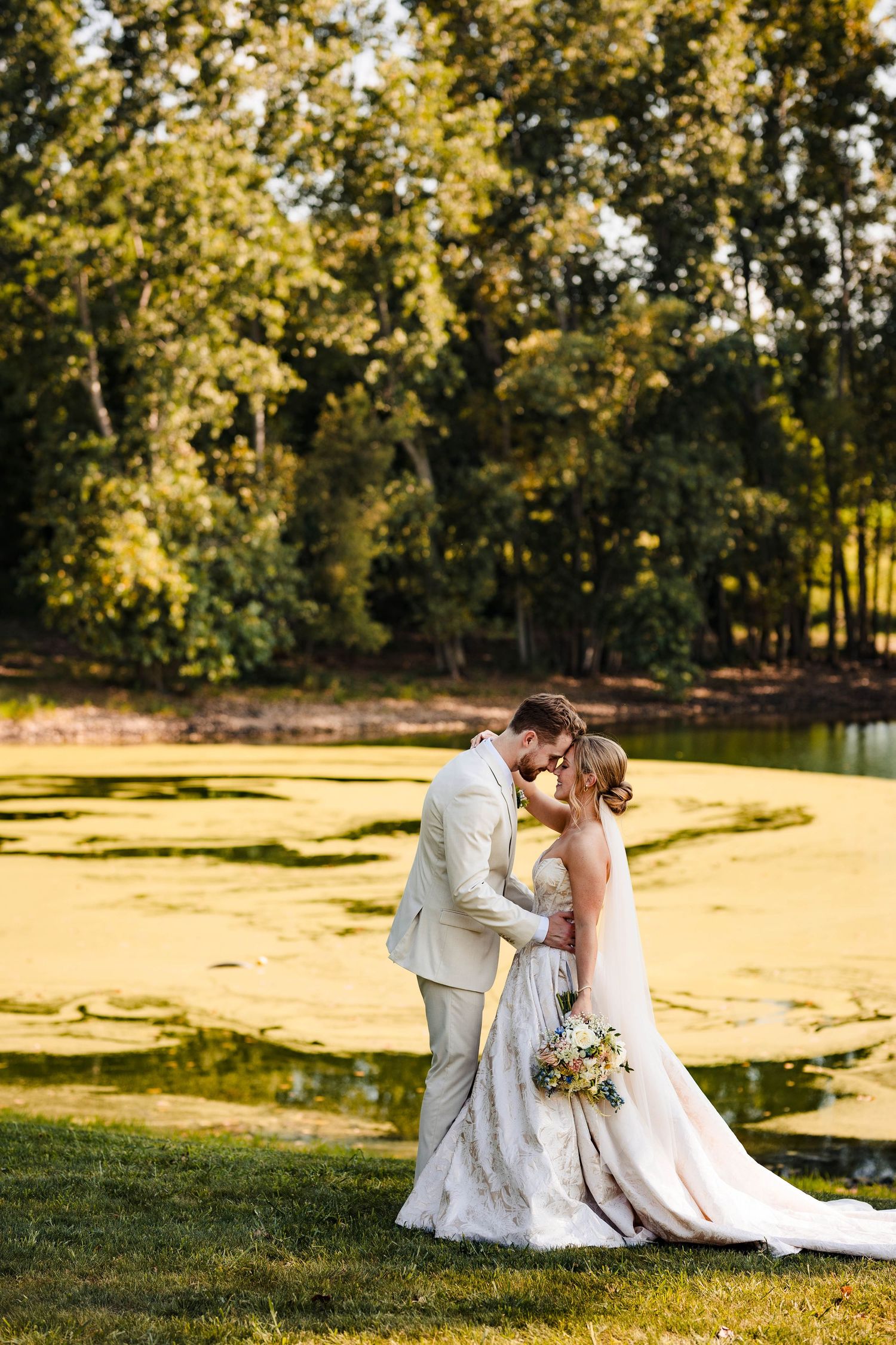 Romantic sunset wedding photos with couple sitting in golden lit field surrounded by trees.