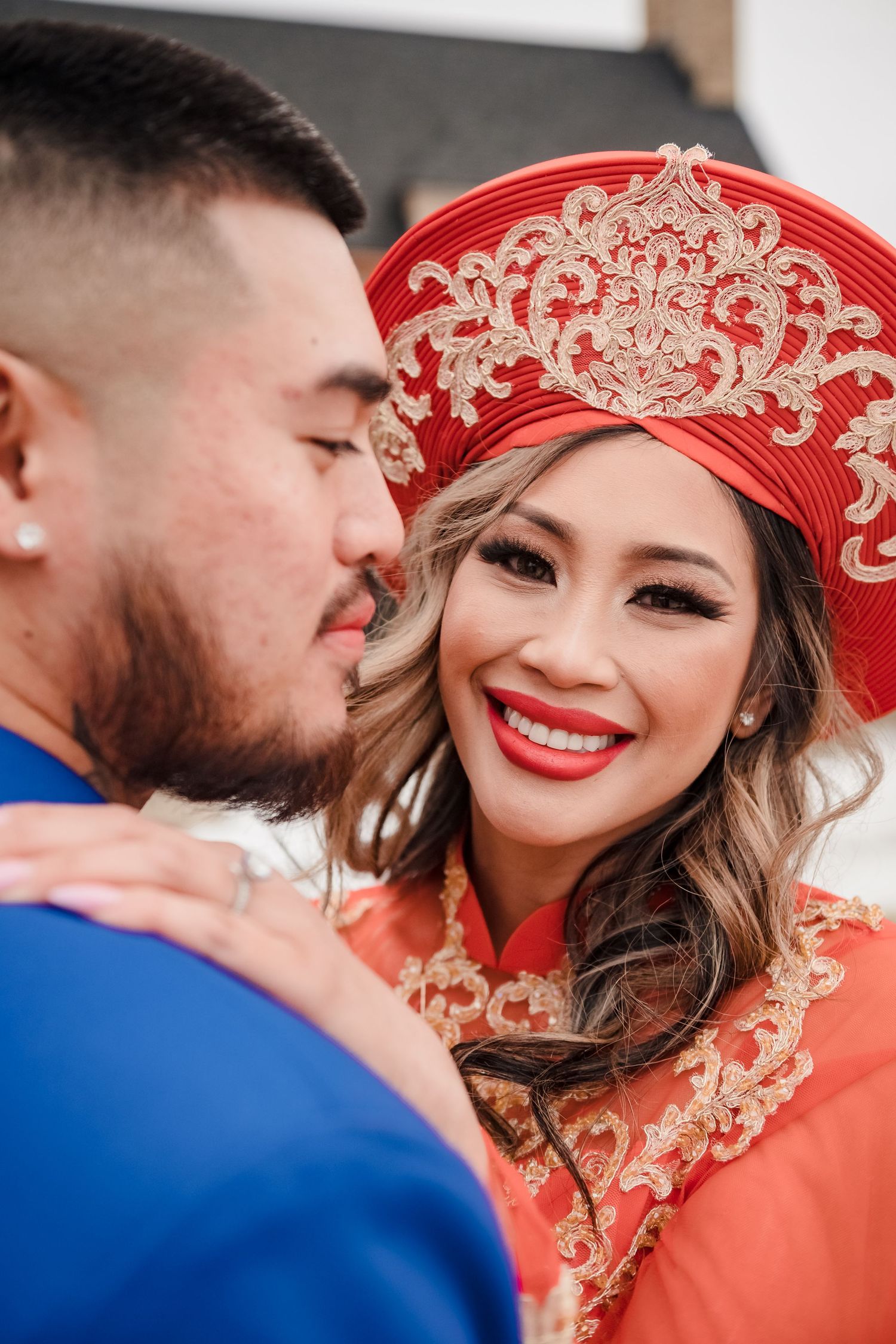 A romantic moment captured in traditional Vietnamese wedding attire featuring a red ao dai and ornate headdress.