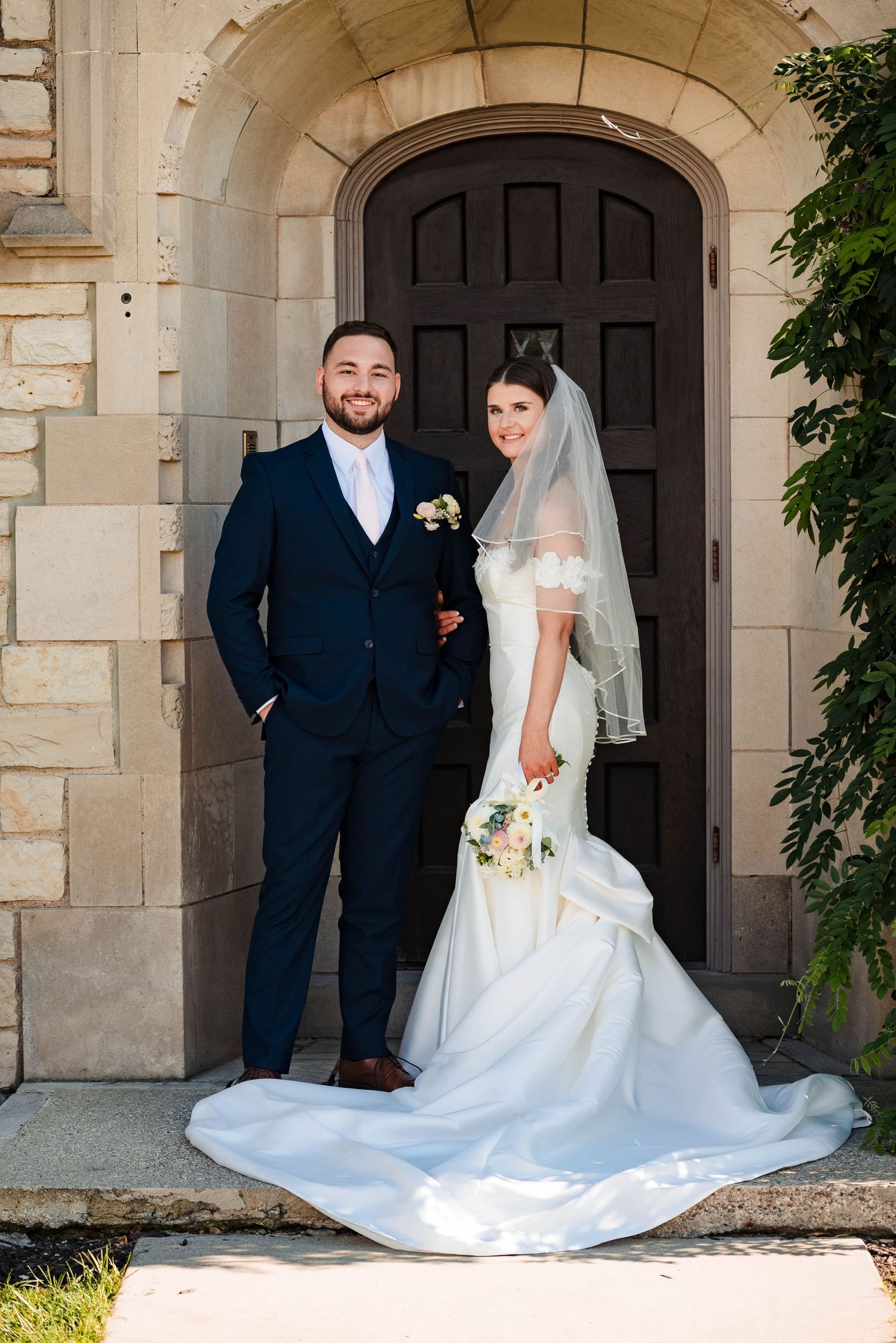 Wedding portraits under elegant stone archway with trailing white dress.