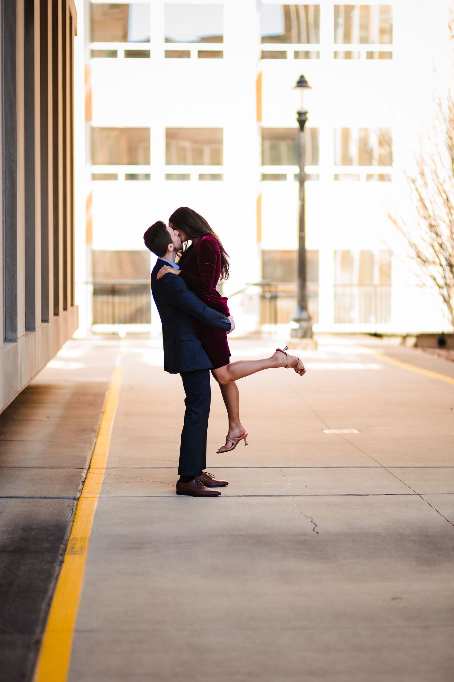 Romantic couple embraces in a sunlit parking garage with dramatic shadows and yellow lines on the ground.