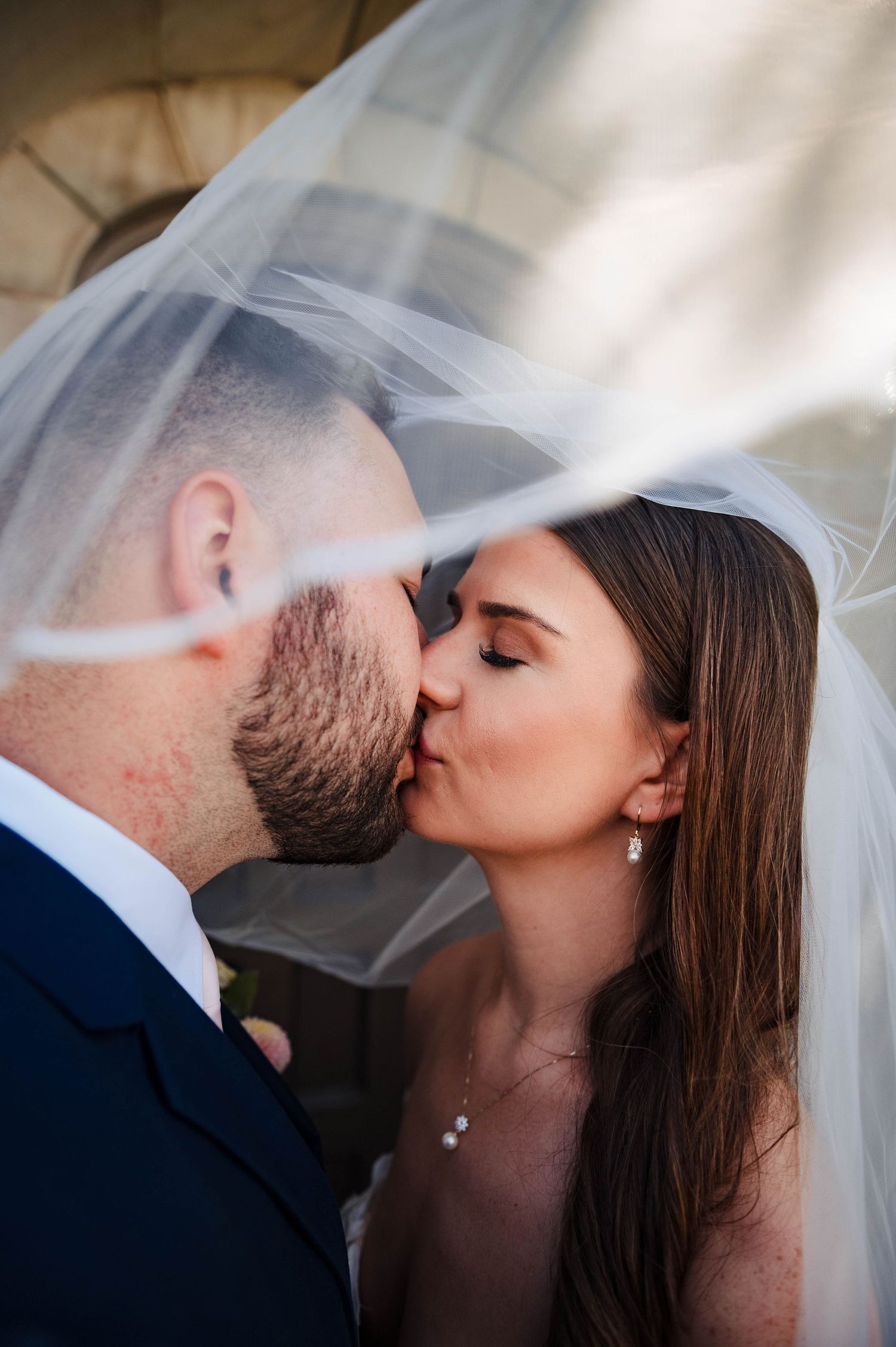 A romantic wedding kiss sequence under a delicate white veil against a soft blurred background.