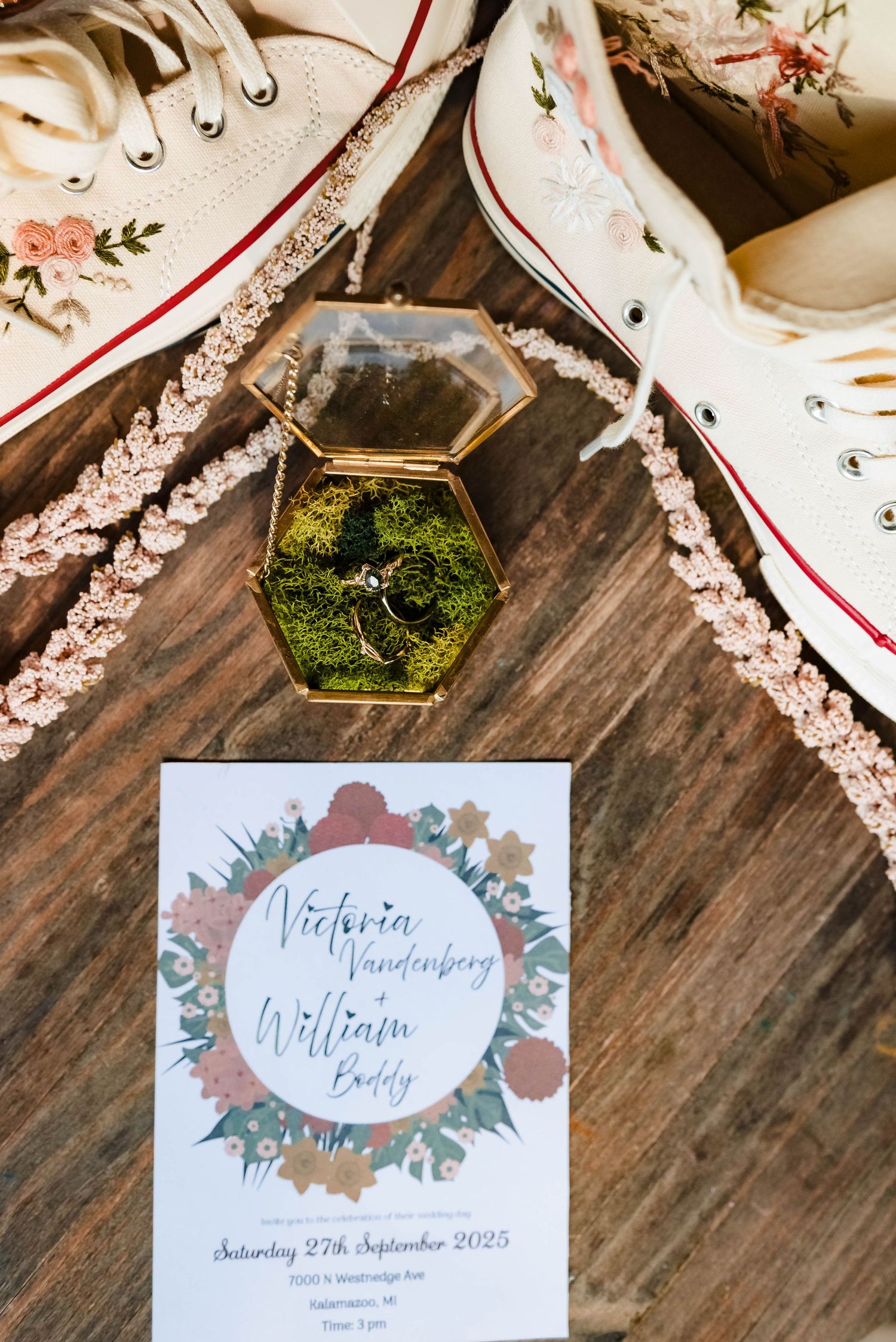 Wedding details with floral invitation, decorated Converse sneakers, and moss-filled hexagonal ring box.