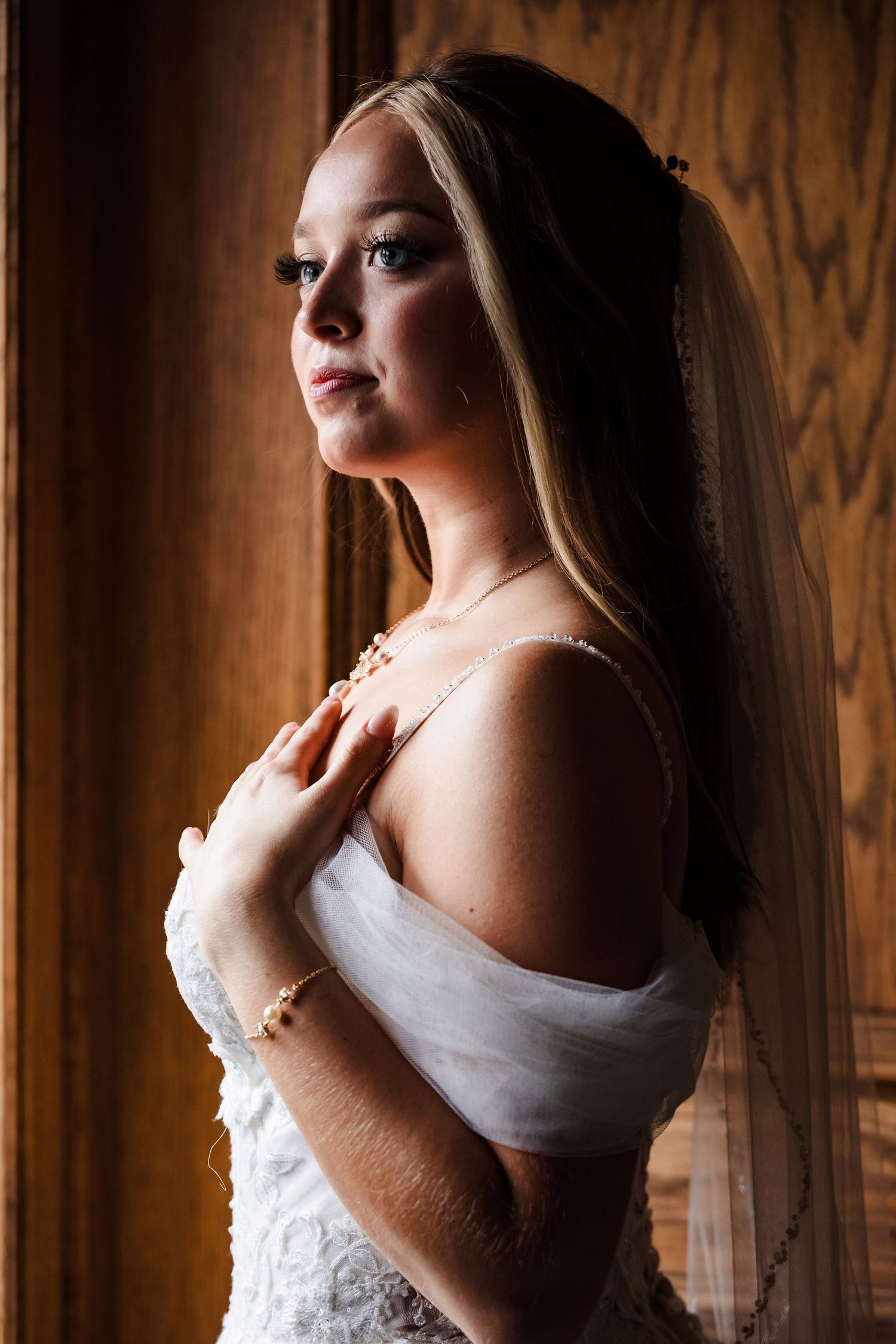 Dramatic side-lit bridal portrait against wooden paneled wall.