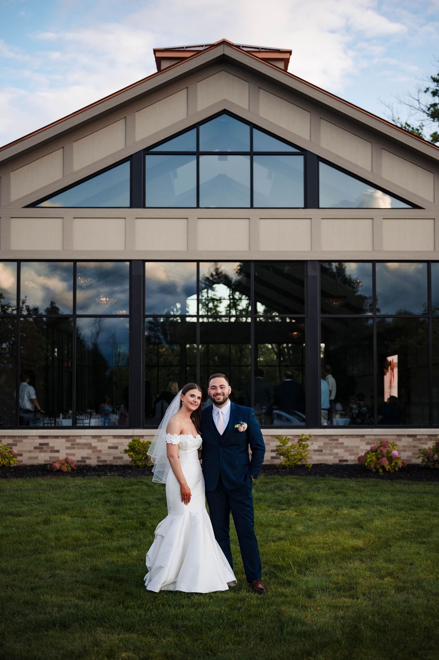 A wedding portrait in front of a modern venue with dramatic triangular windows.