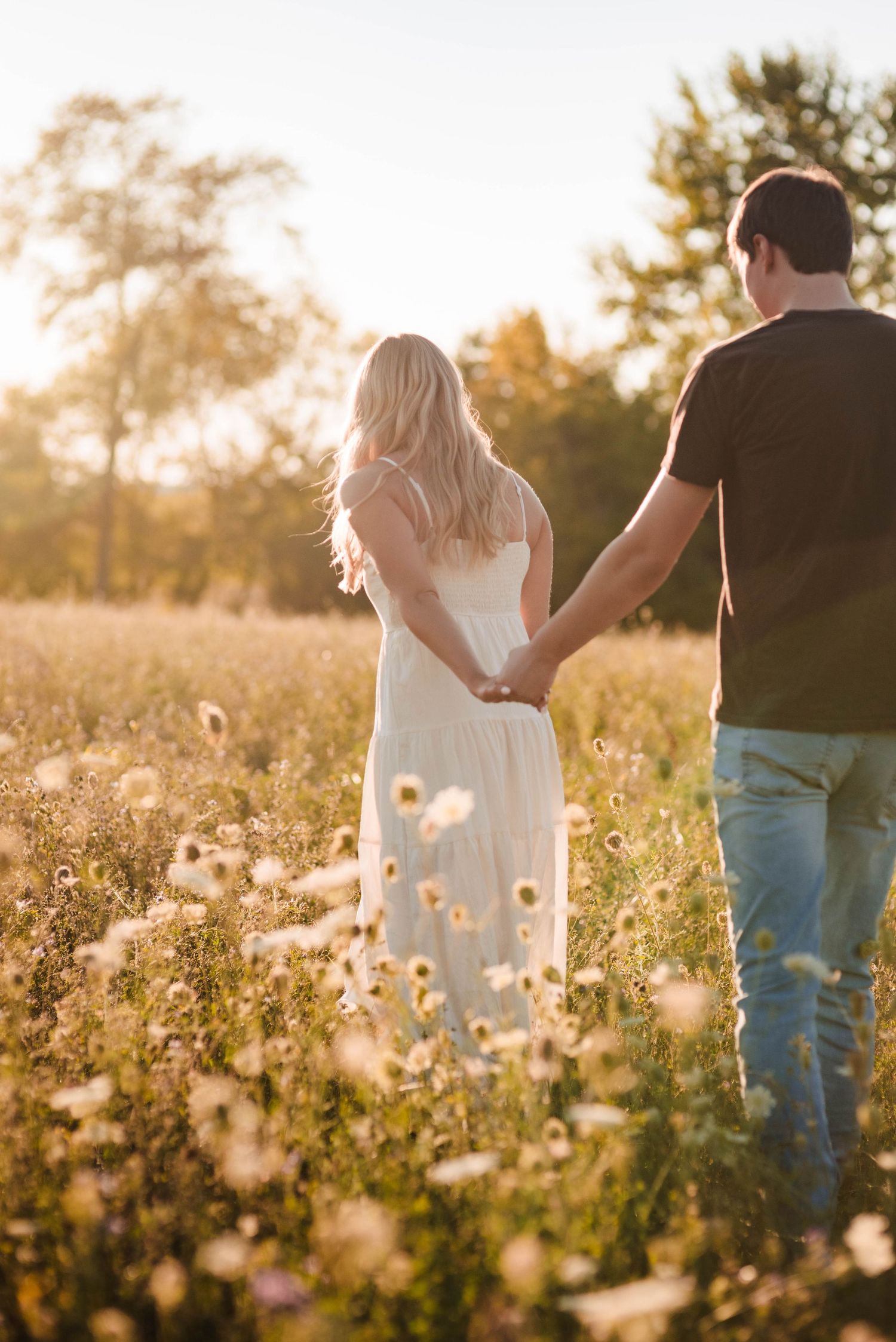 Couple walking through sunlit meadow with wildflowers at golden hour.