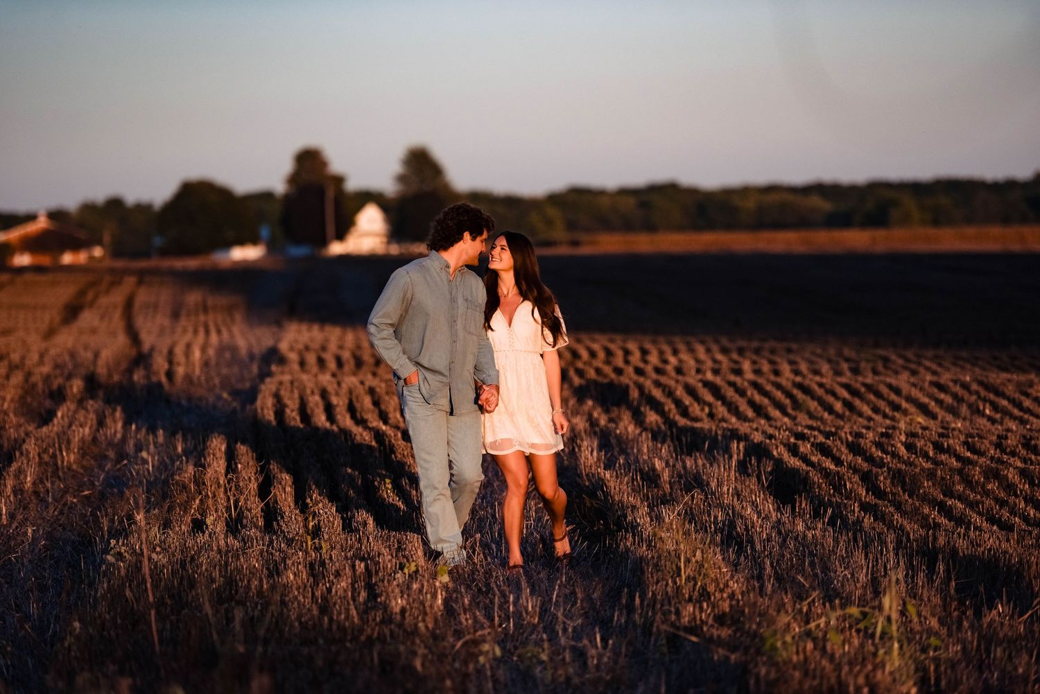 Silhouettes of a couple walking through a harvested field at sunset.