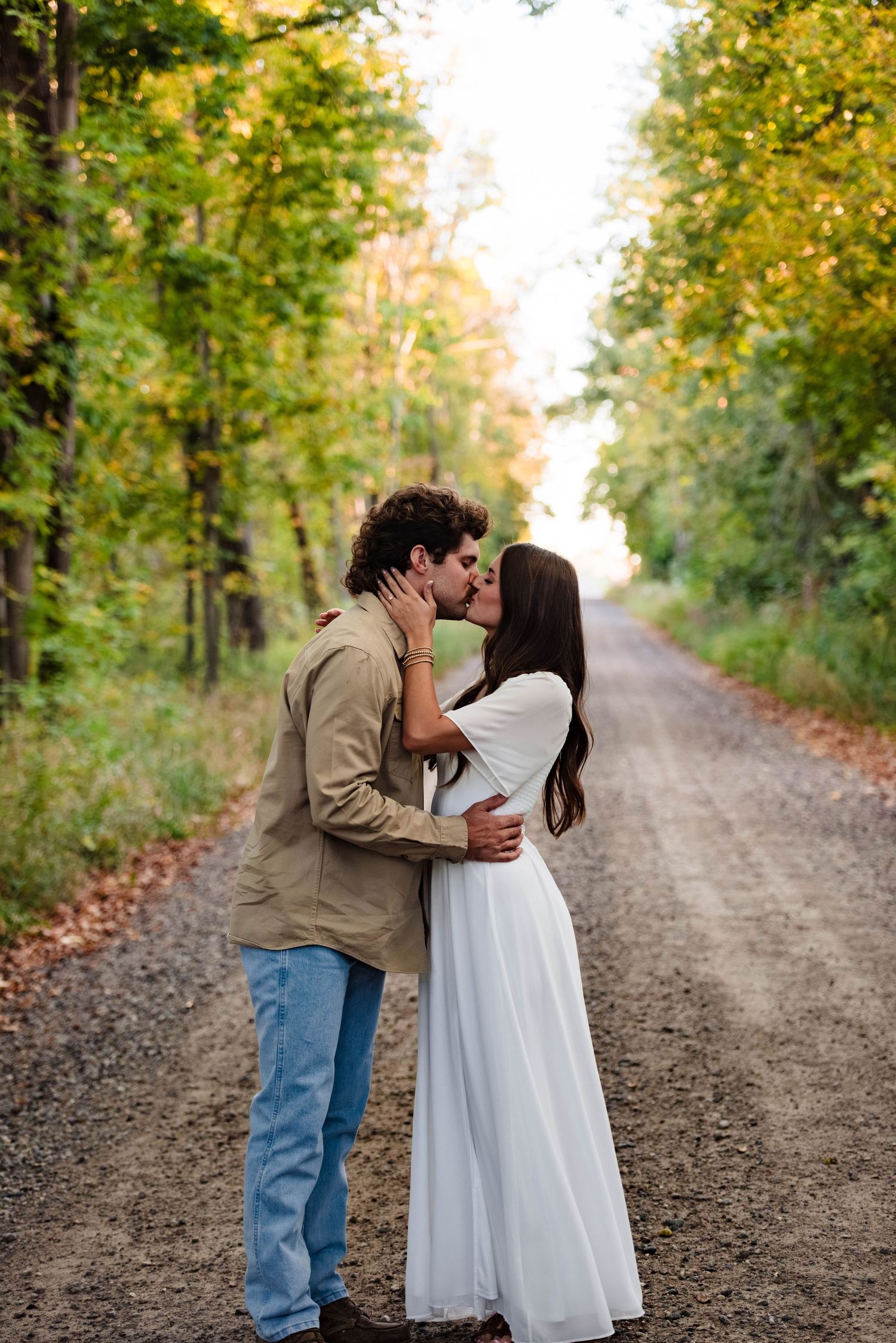 A romantic couple shares tender moments on a tree-lined dirt road in autumn.