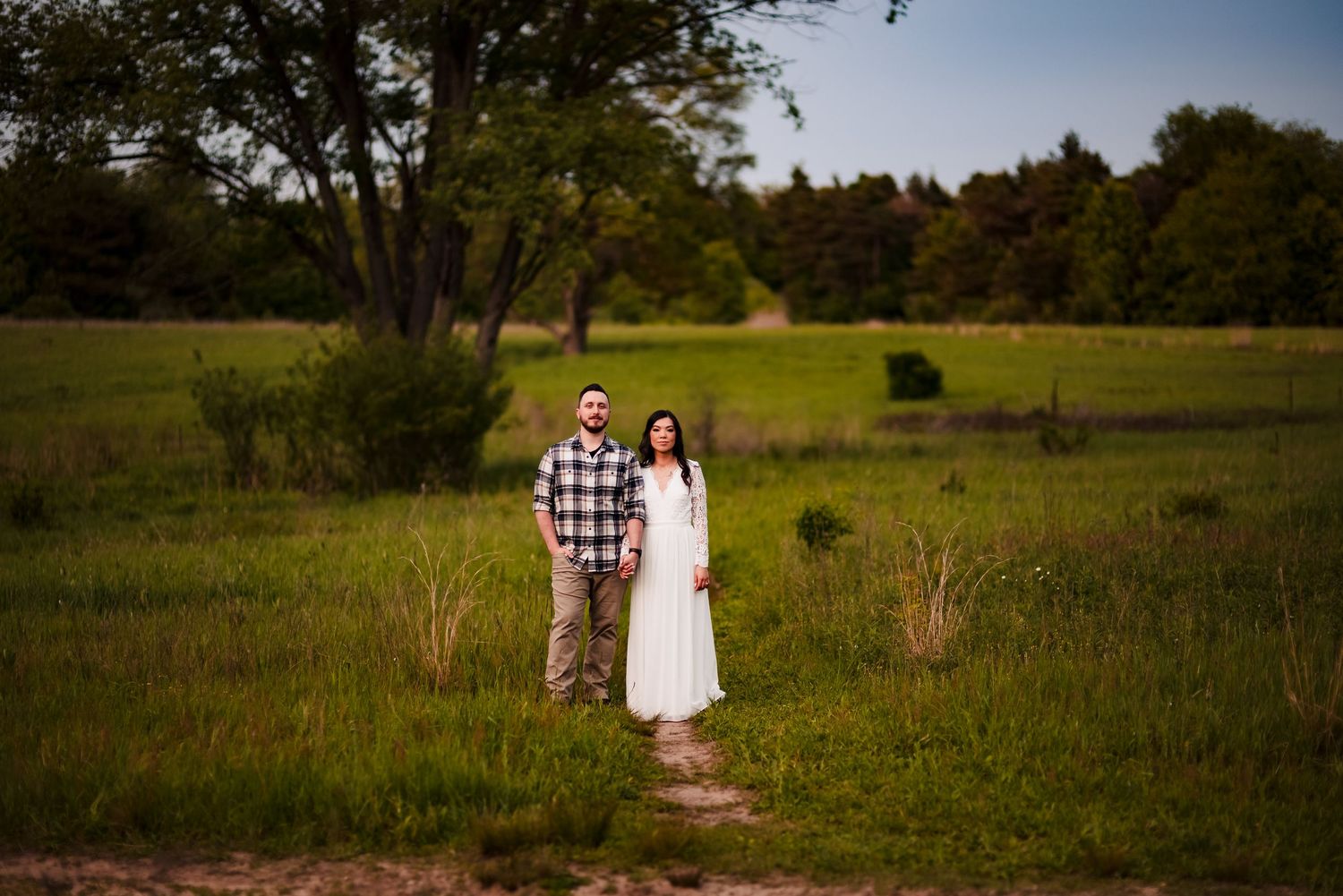 Couple walking through green meadow in casual summer outfits.
