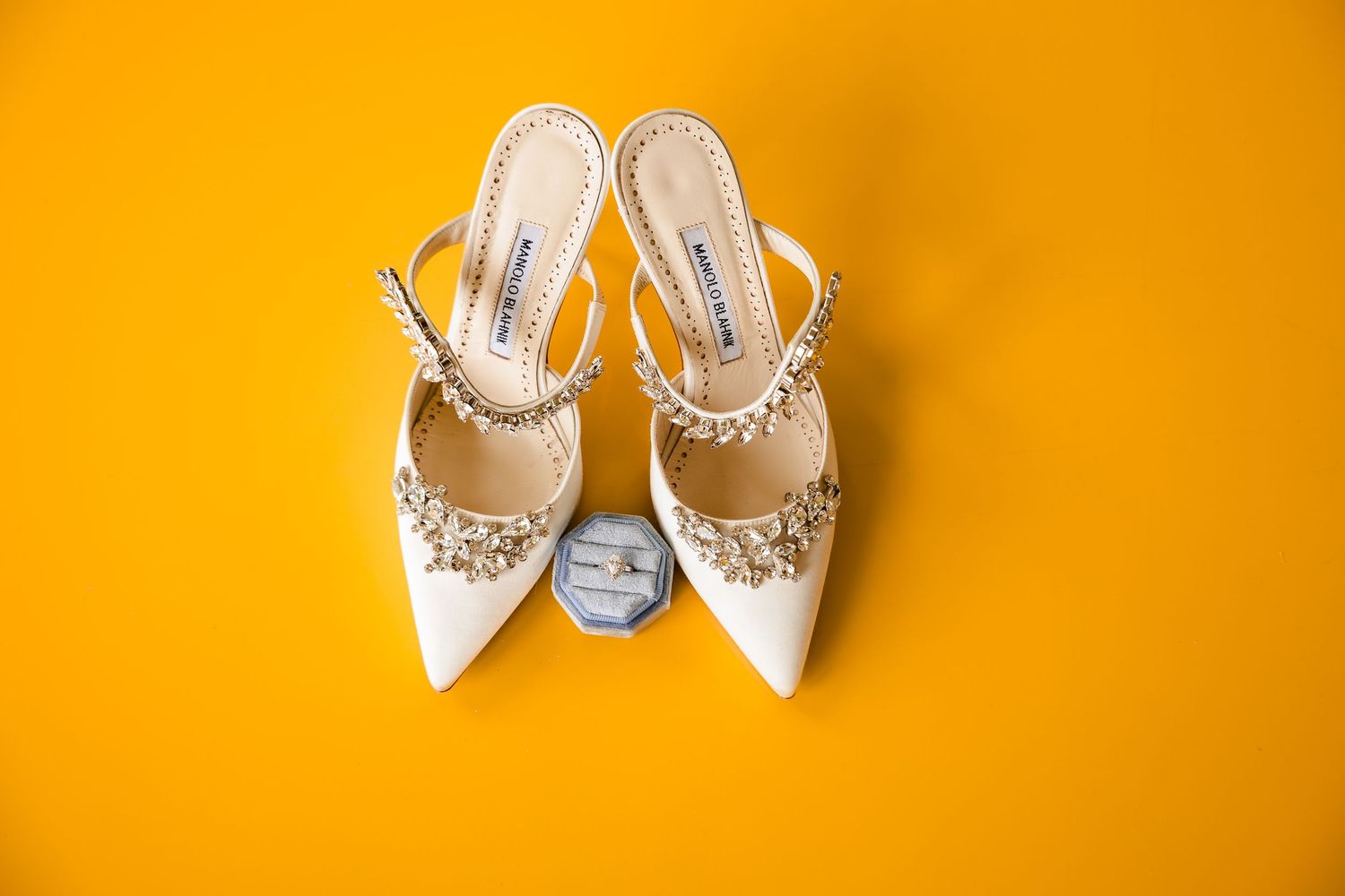 Elegant white bridal shoes with pearl and crystal embellishments displayed on a bright orange background.