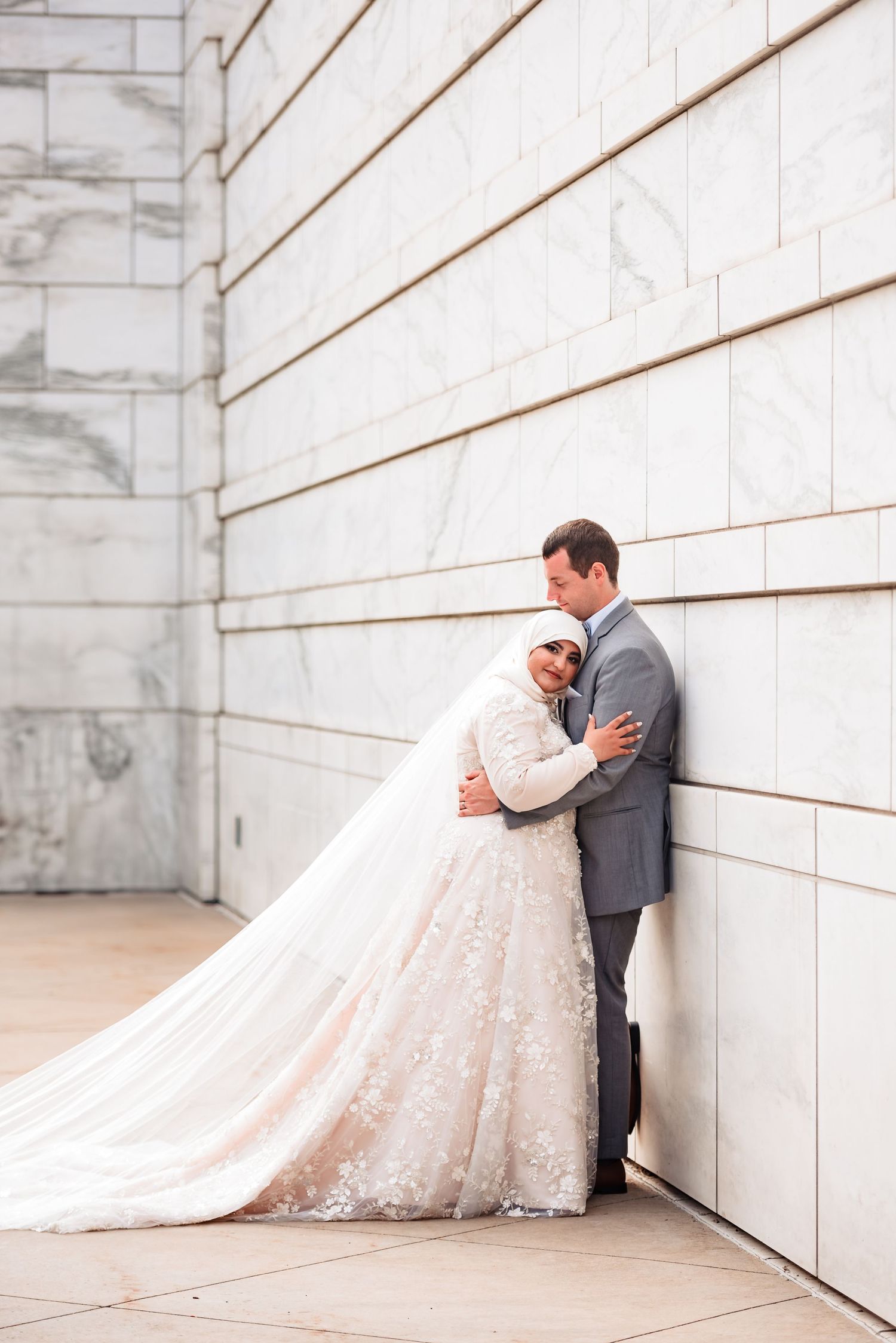 A romantic wedding photo series showing a couple embracing against a white marble wall with diagonal wood accents.