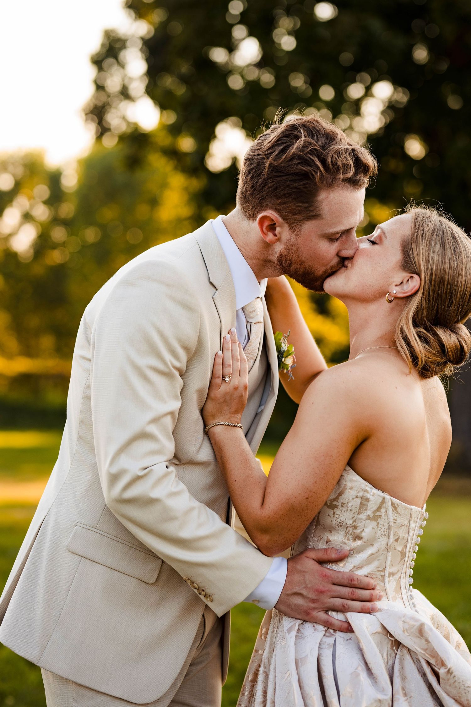 Romantic wedding couple shares intimate kisses in a sunlit garden setting wearing beige and white attire.
