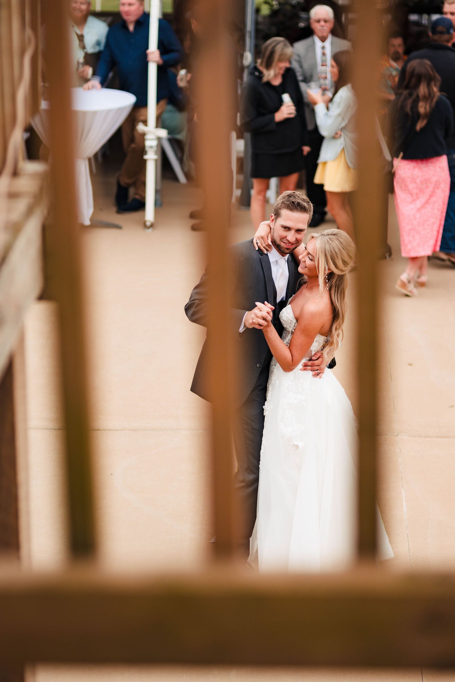 Wedding celebration glimpses seen through wooden pillars in an indoor venue.