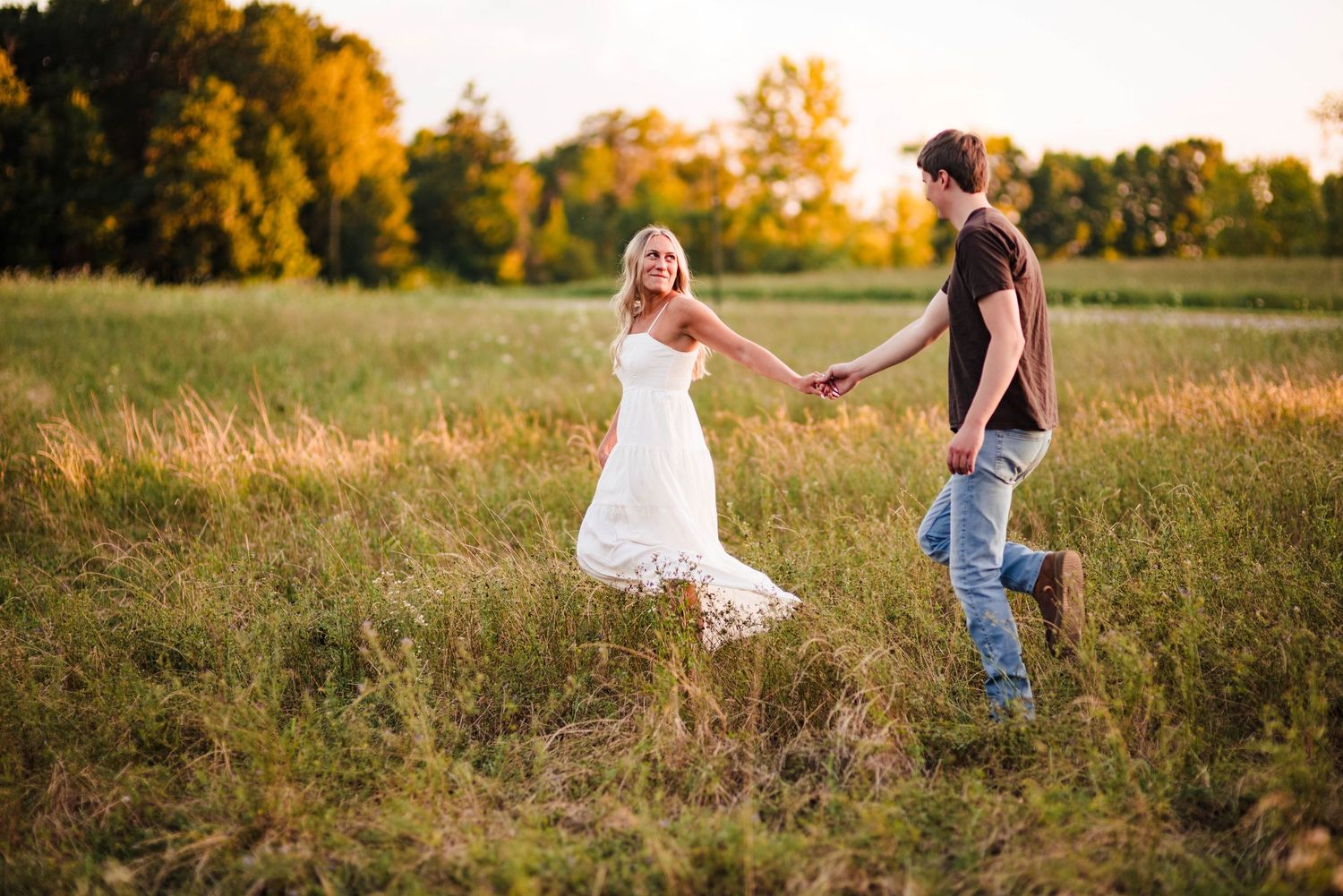 Couple walking through a sunlit meadow during golden hour.