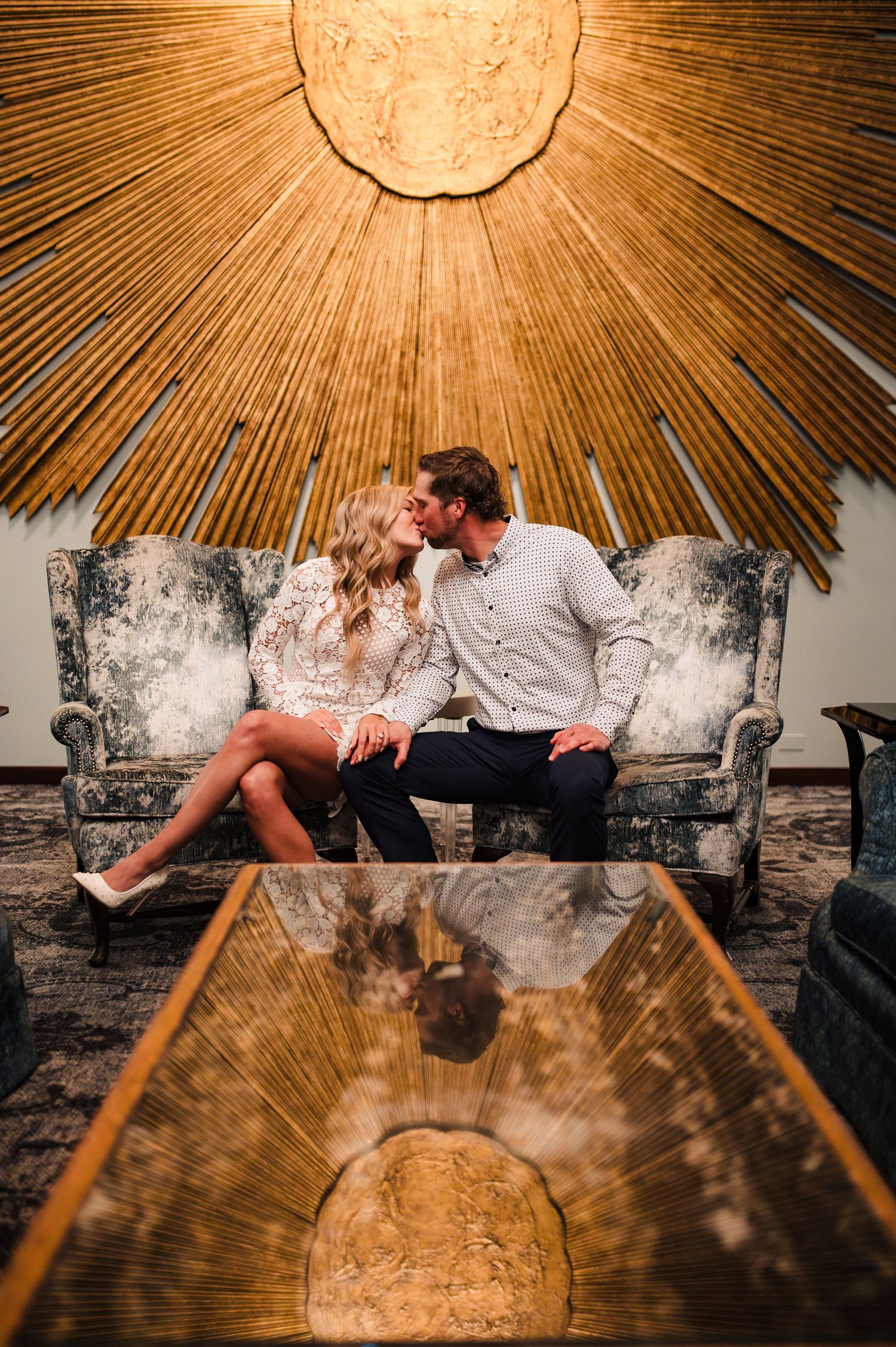 Artistic couple portrait under a sunburst ceiling with vintage couch and dramatic lighting.