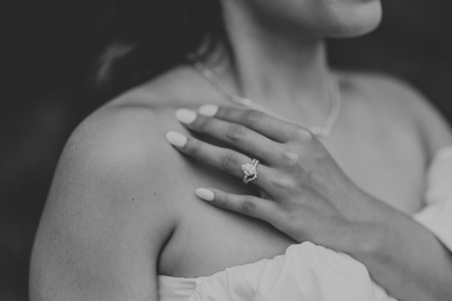Black and white close-up of hands wearing an engagement ring against a white dress.