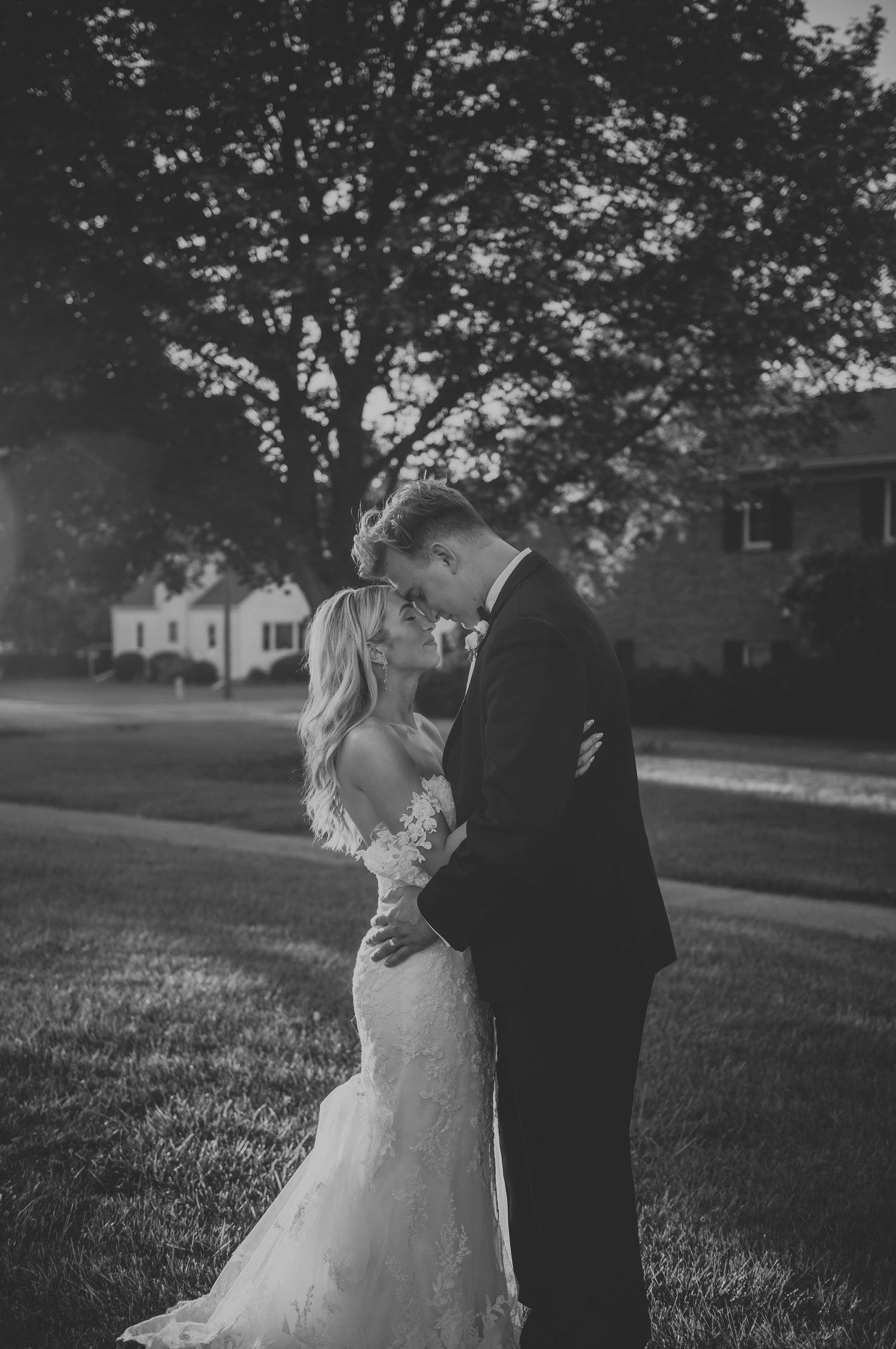 A romantic black and white wedding photo sequence showing a couple embracing on a grassy lawn with trees in background.