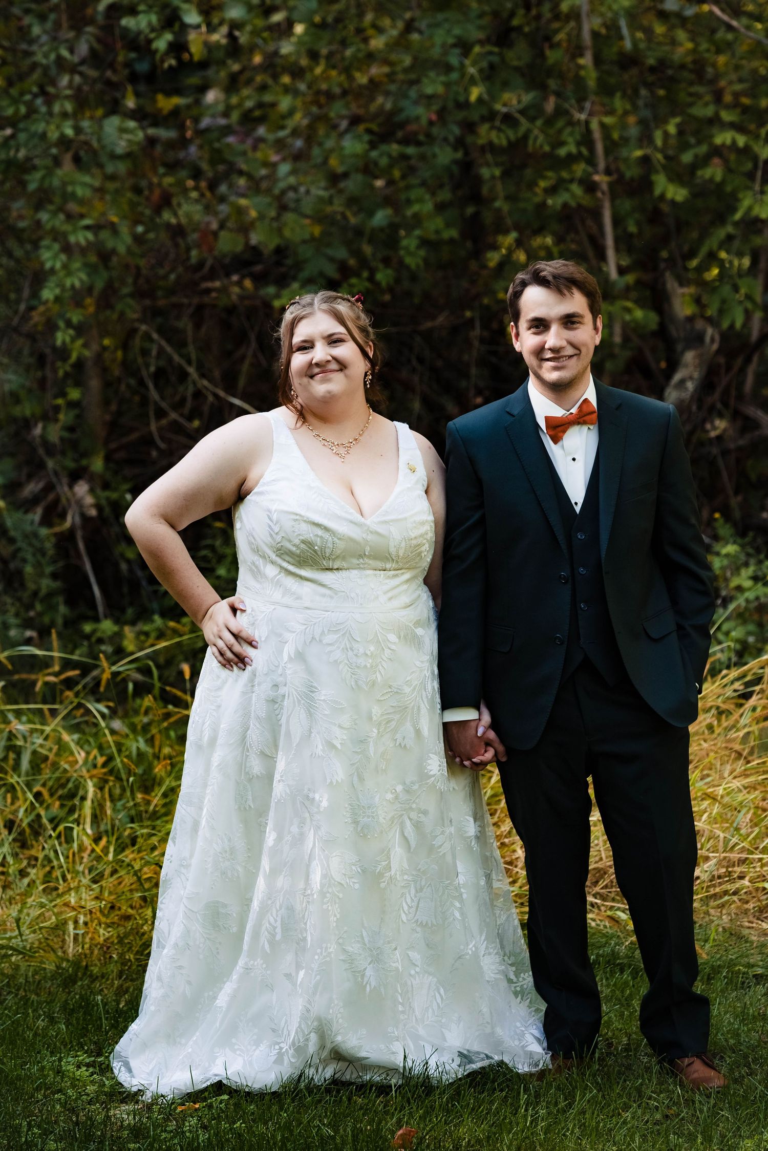 Wedding couple poses together in a natural outdoor setting with fall foliage.