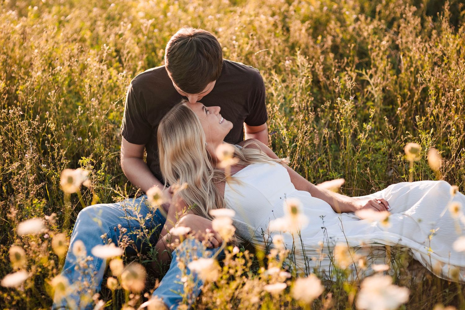 Couple lying together in golden wildflower field during sunset.