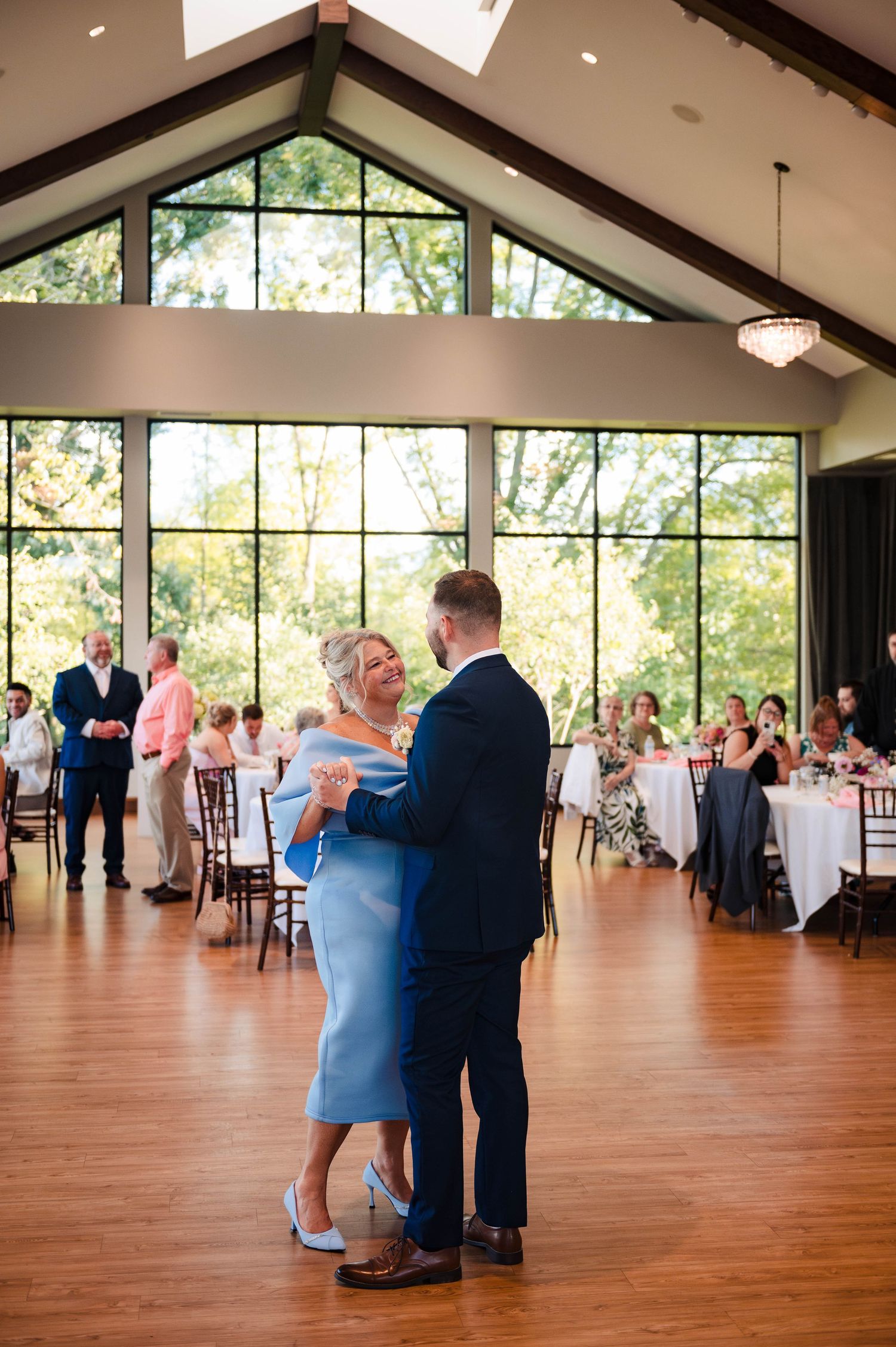 A couple shares their first dance in an elegant reception hall with vaulted ceilings and large windows.
