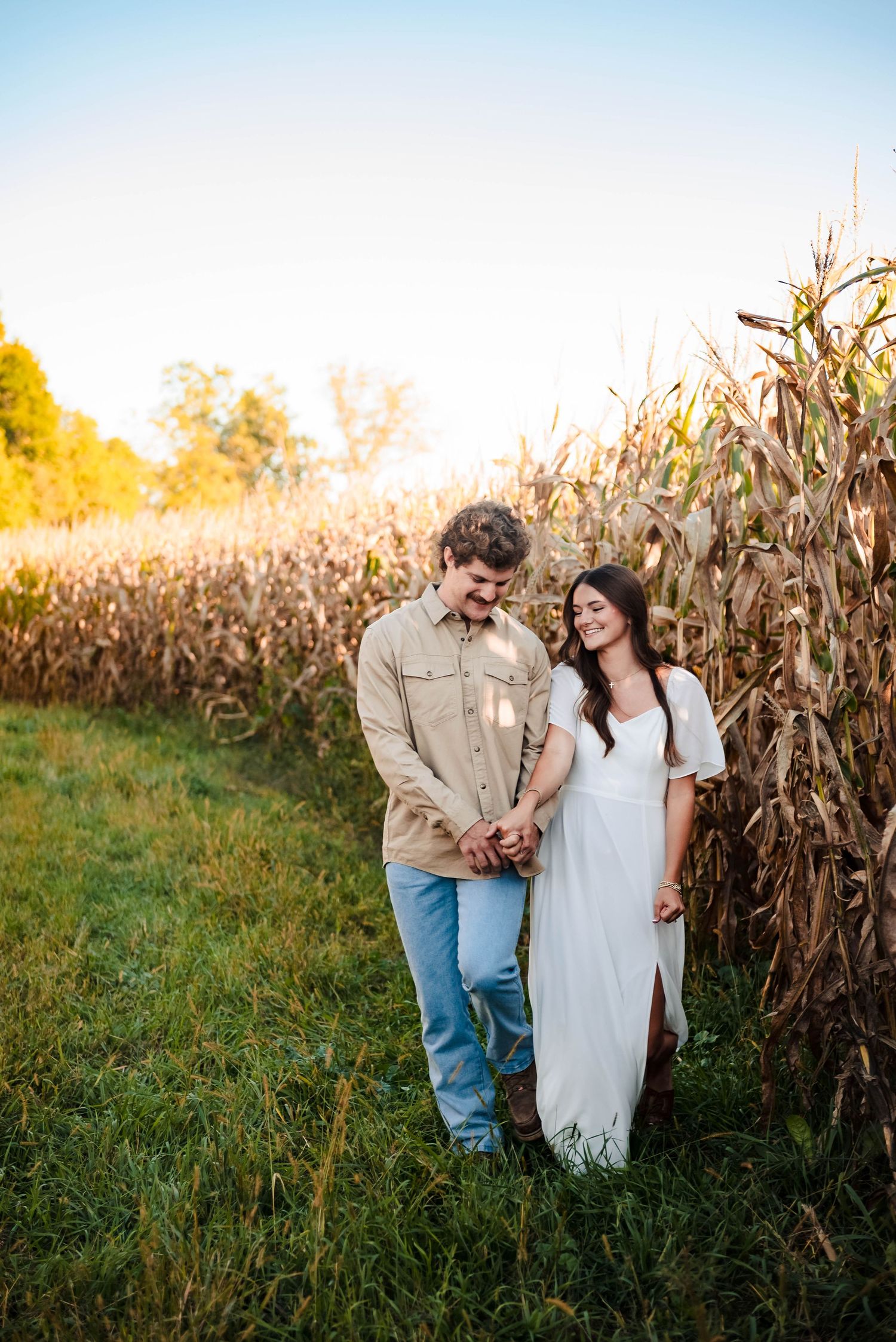 Couple shares intimate moment at edge of cornfield during golden hour.
