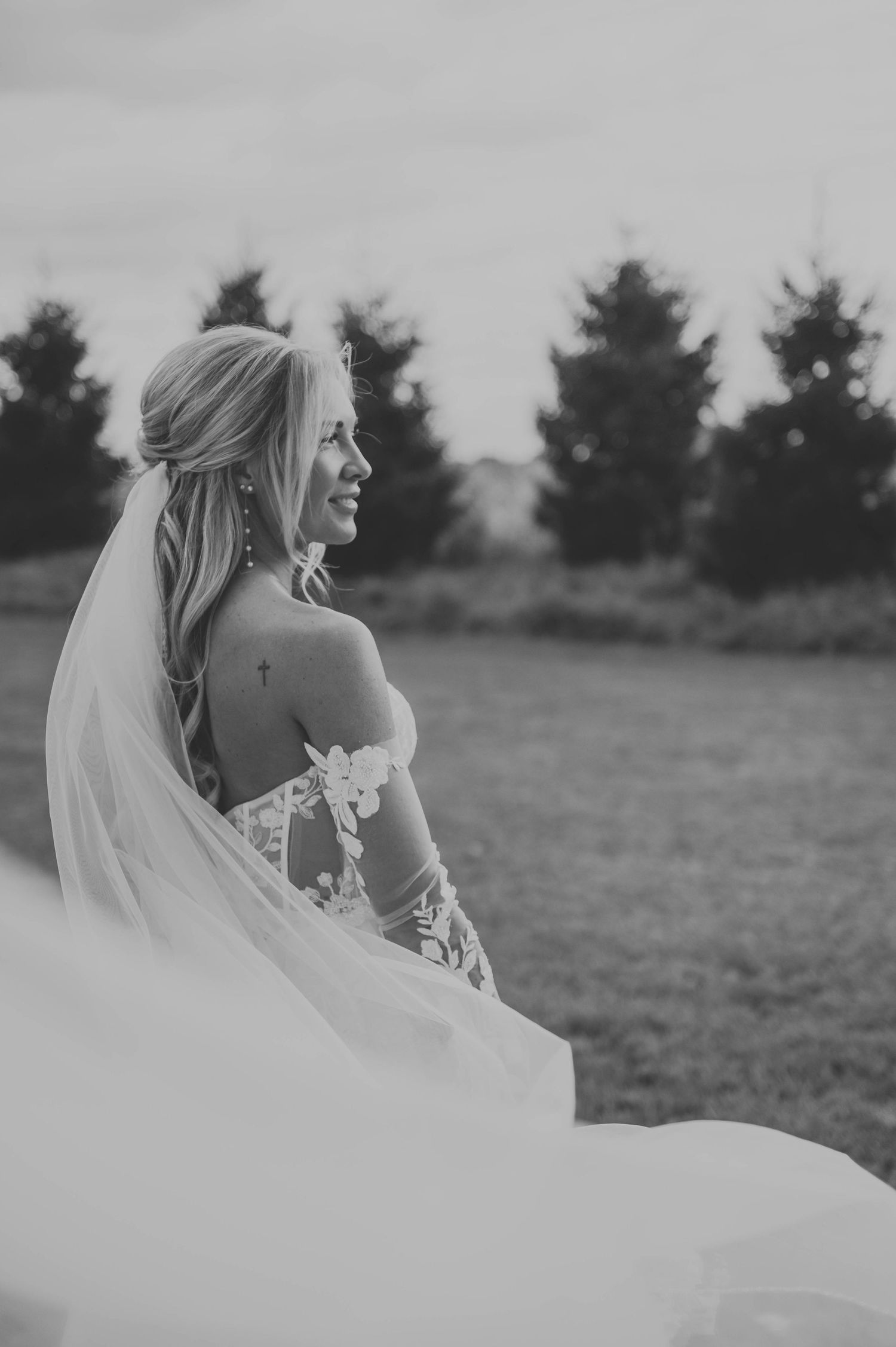 Black and white portrait of bride with flowing veil against natural landscape.