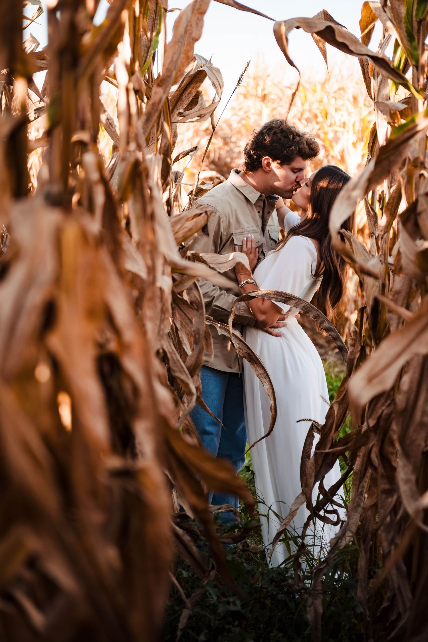 Intimate moment between couple among tall dried corn stalks in autumn field.