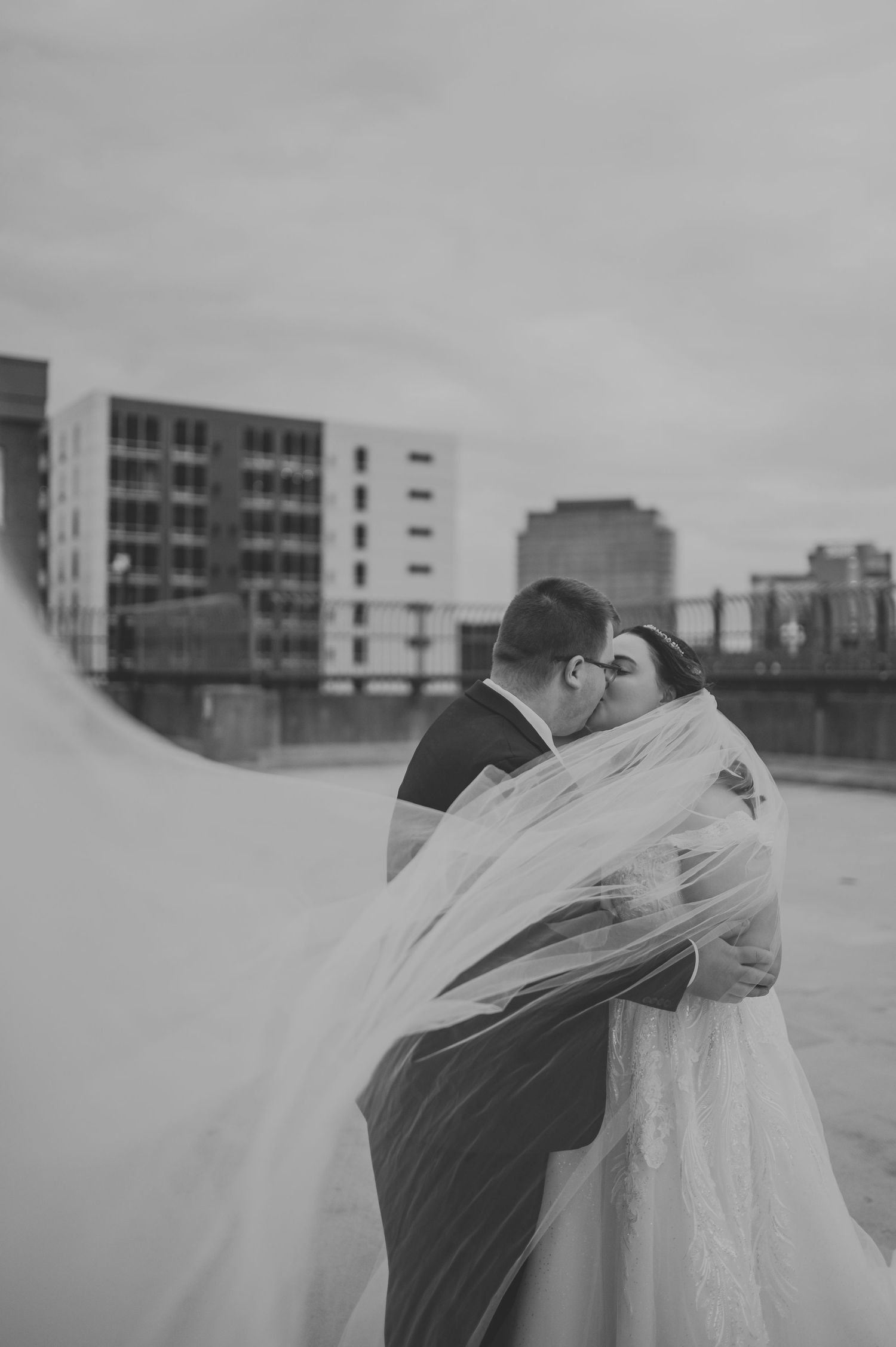 A romantic black and white sequence of a couple embracing under a flowing veil on a rooftop.