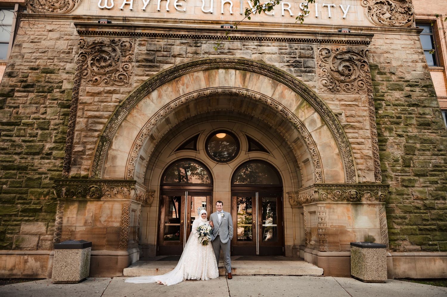 Elegant wedding couple stands beneath a stone archway entrance of a historic church building.