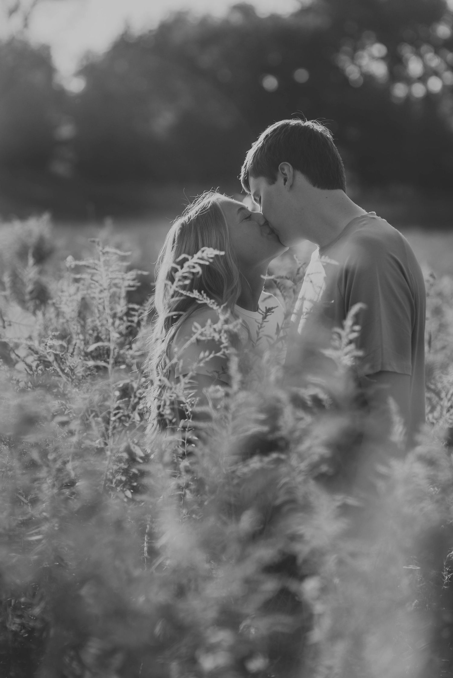 Black and white photo of couple embracing in tall grass field.