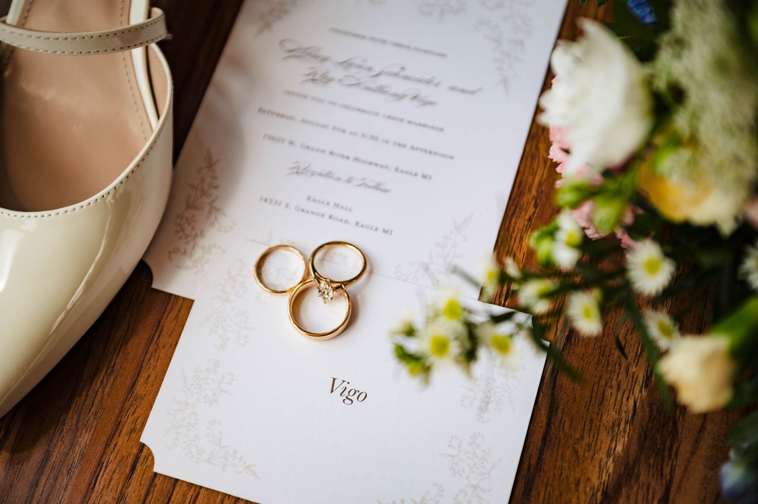 Wedding rings and invitation details artfully arranged on wooden surface with soft lighting.