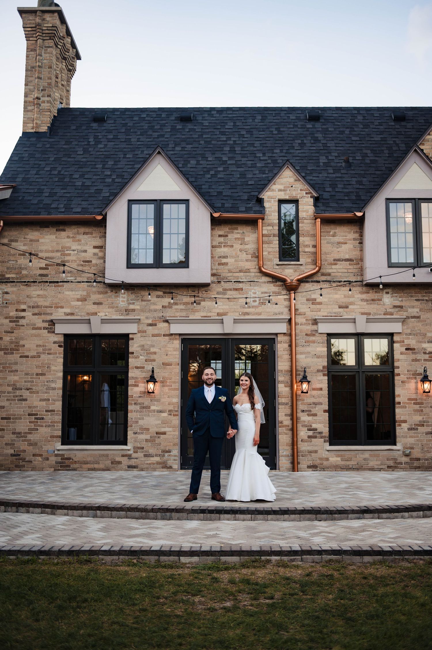 A wedding portrait in front of a Tudor-style brick venue with dormers and black trim.
