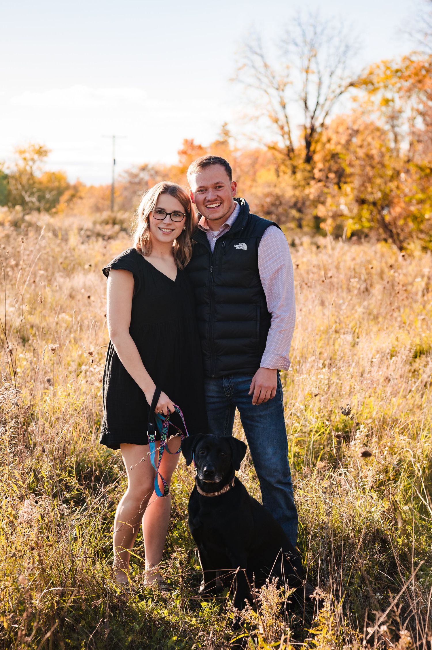 A couple shares intimate moments in a golden autumn field during sunset, surrounded by tall grass and fall foliage.