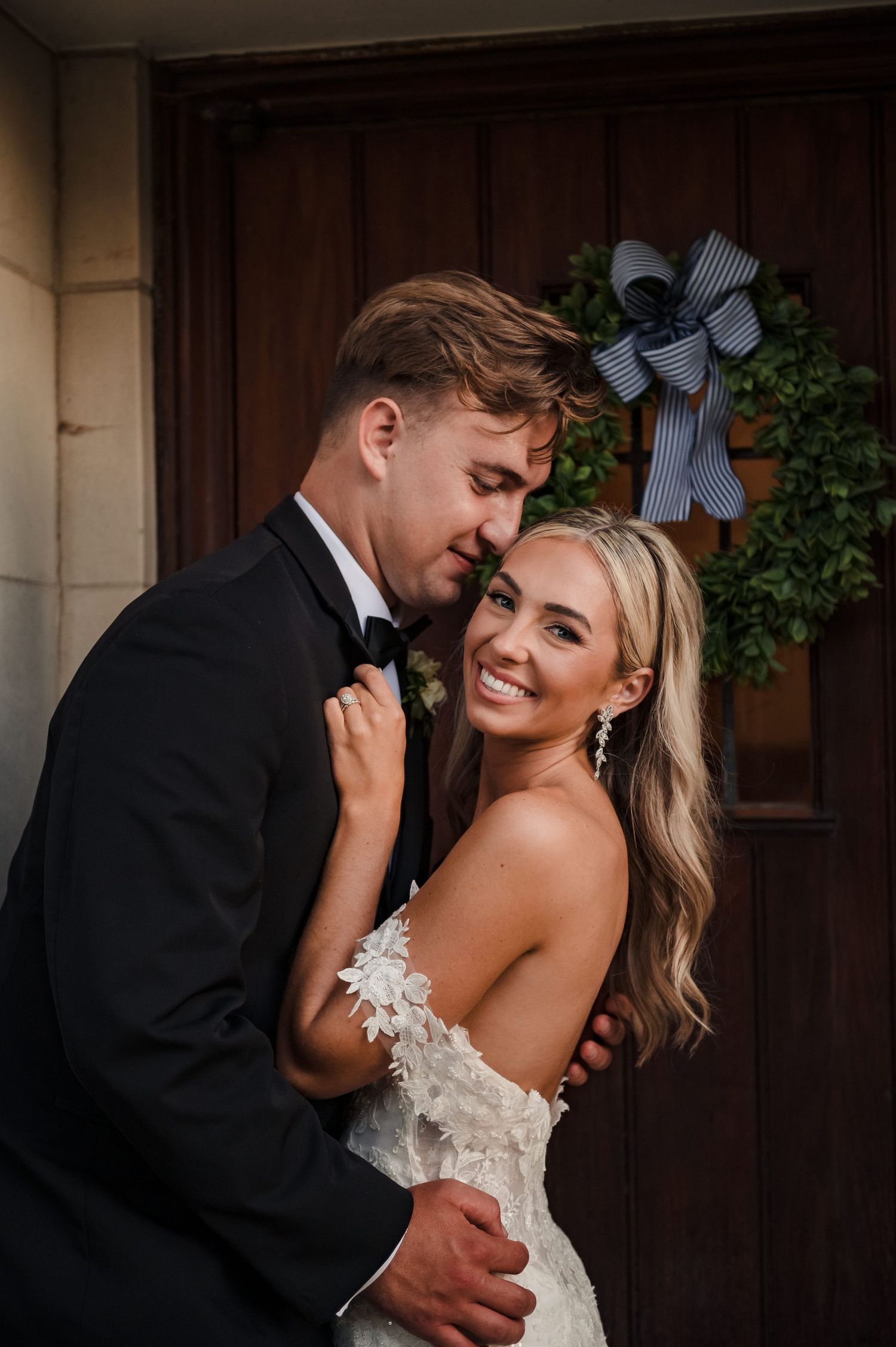 A joyful couple shares intimate moments and laughter against a dark wooden door backdrop at their wedding.