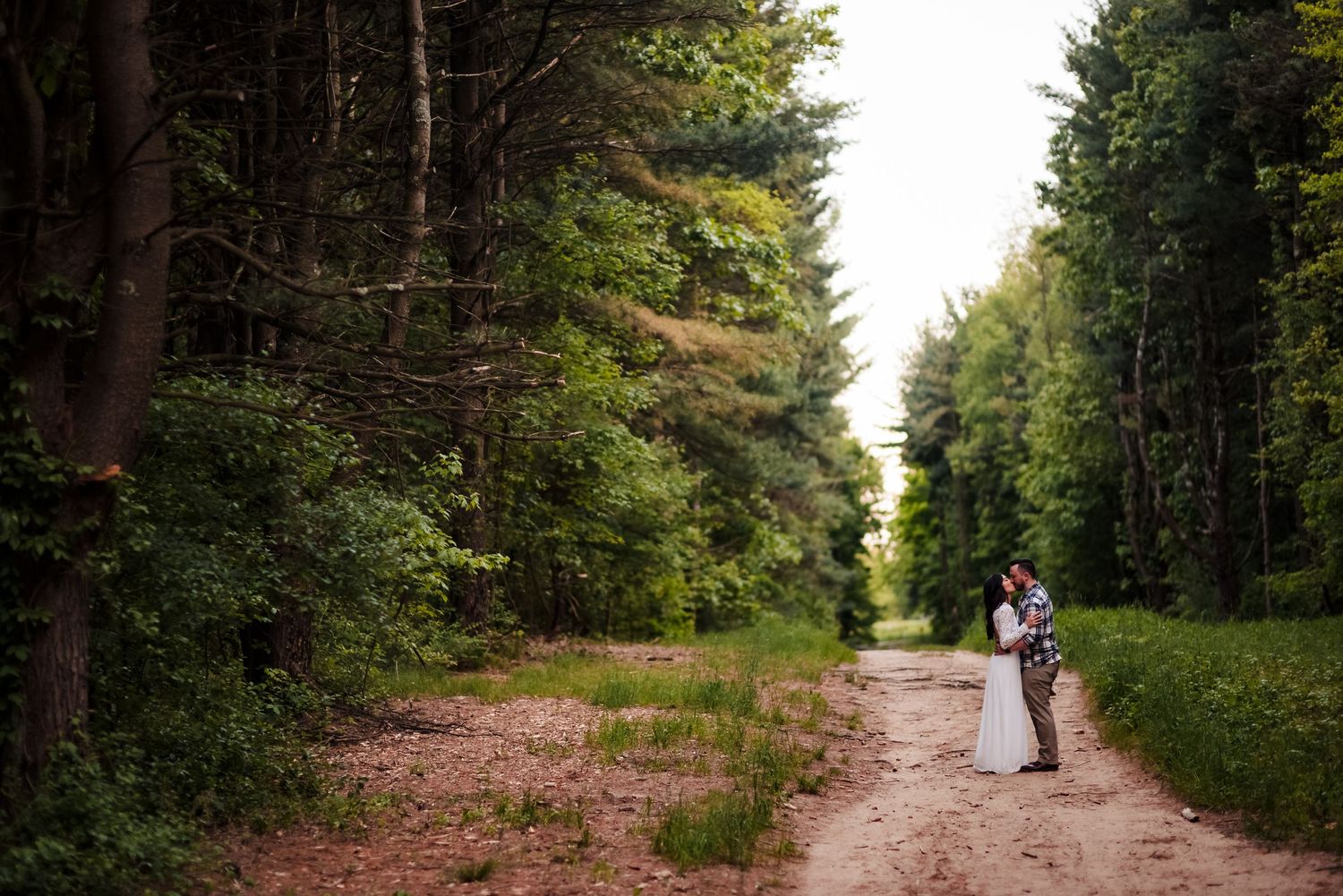 Tree-lined dirt path through forest leading to sunset.