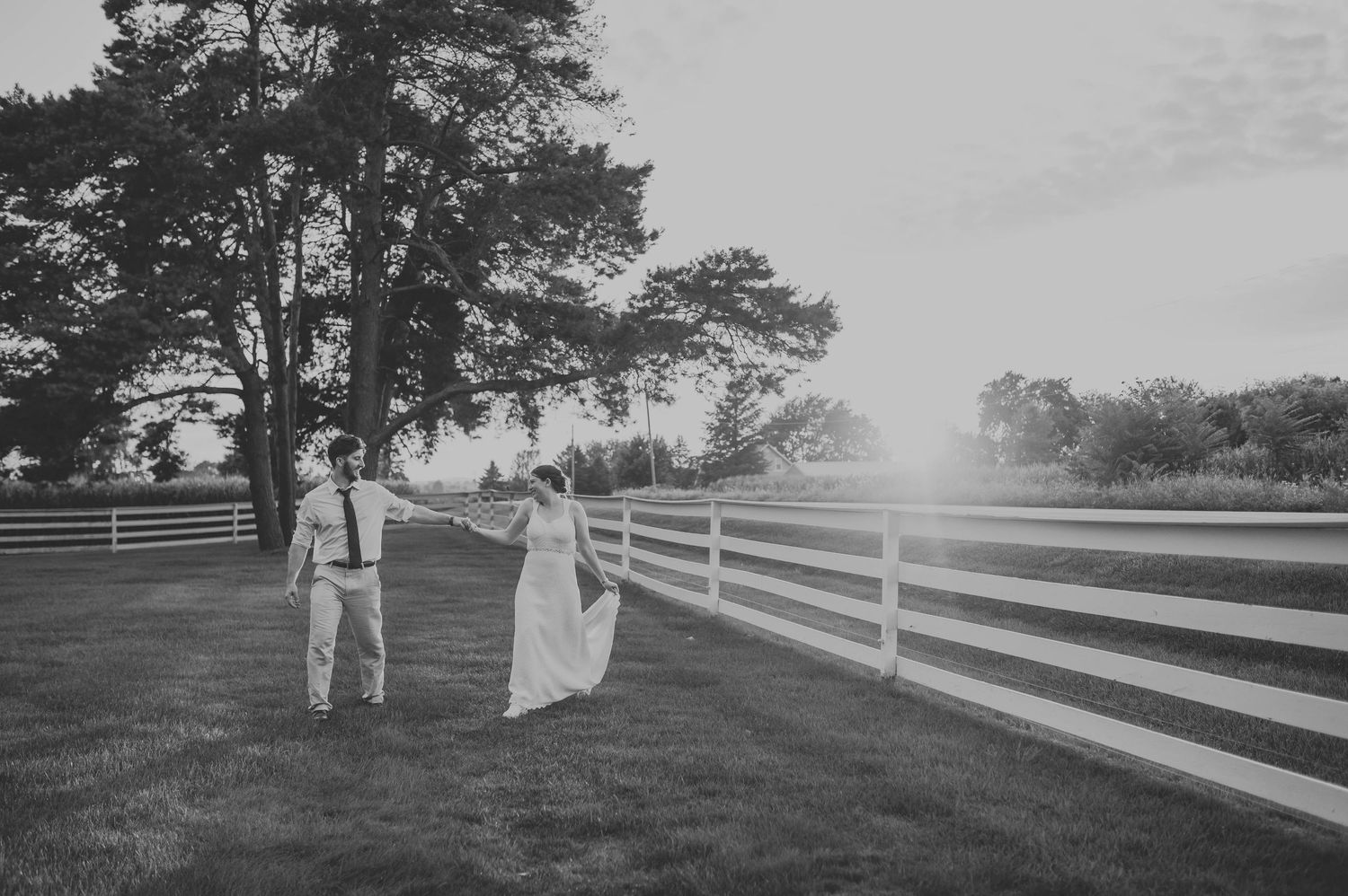 A couple walks along a white fence path in black and white vintage photograph.