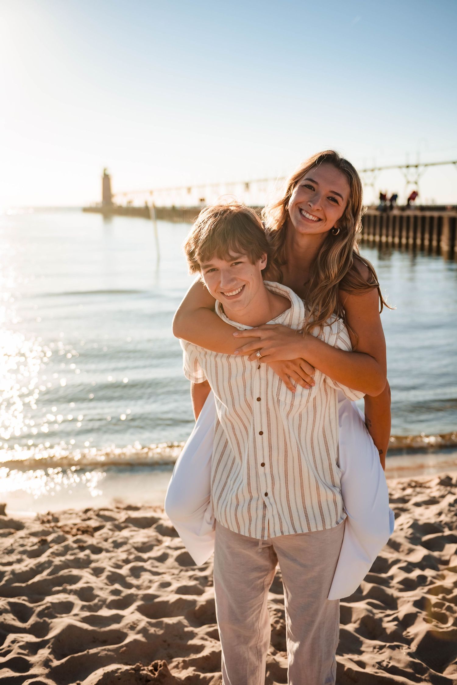 Playful beach photoshoot with couple in white and striped outfits on sandy shore.