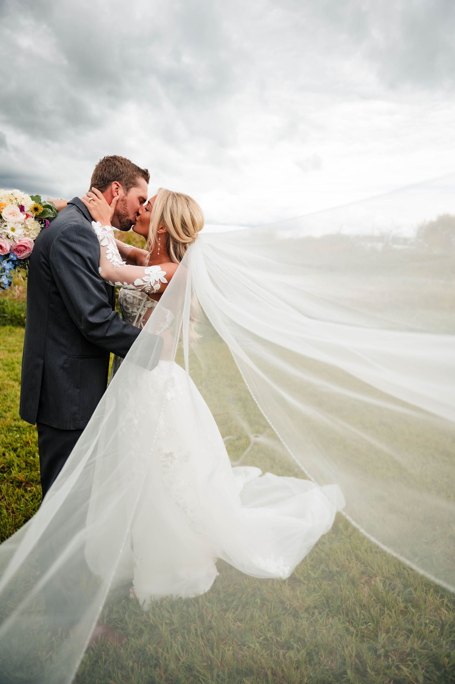 A romantic wedding moment with bride's veil flowing in the wind against cloudy sky.