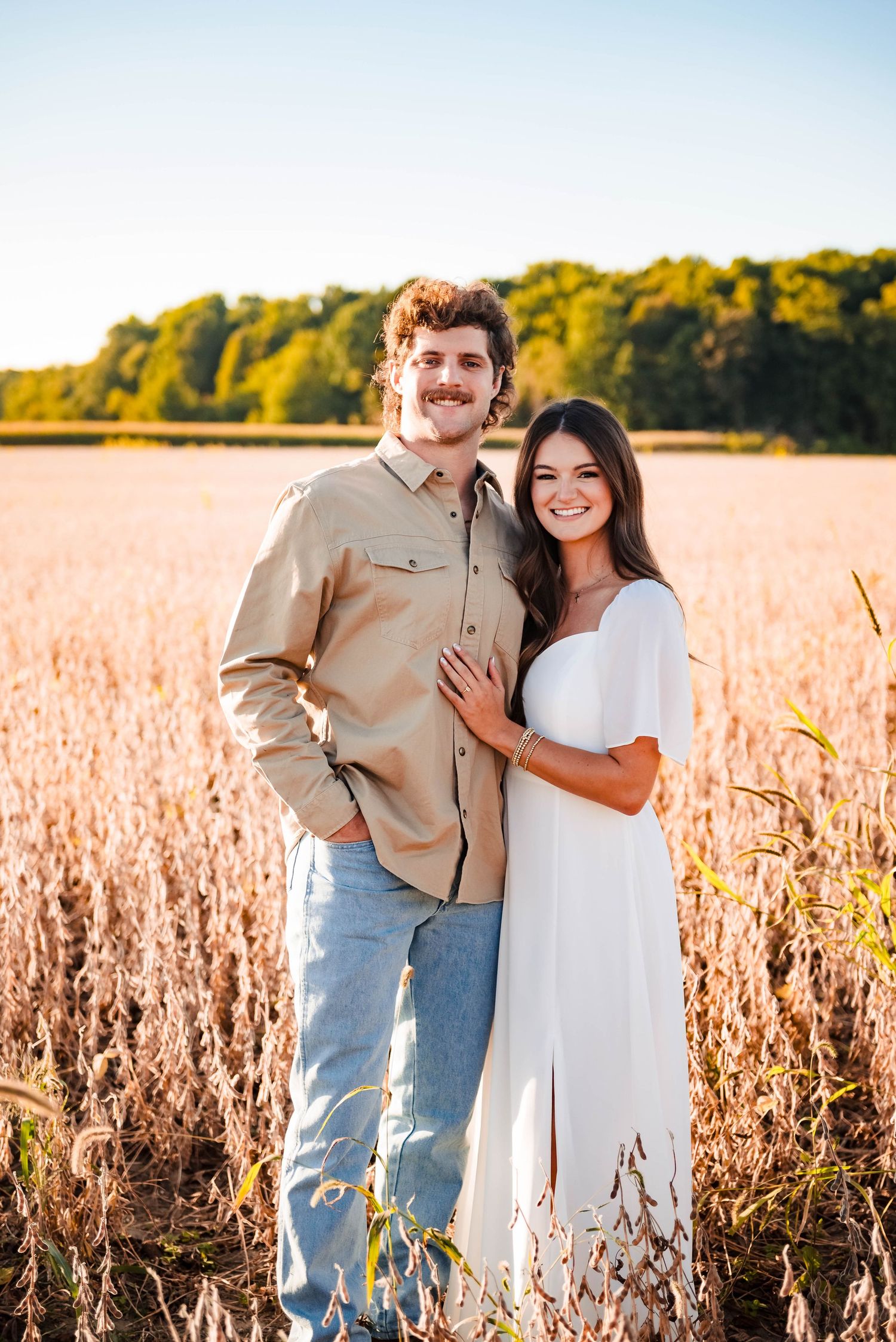 Happy couple posing in a sunlit field of dried soybeans during golden hour.