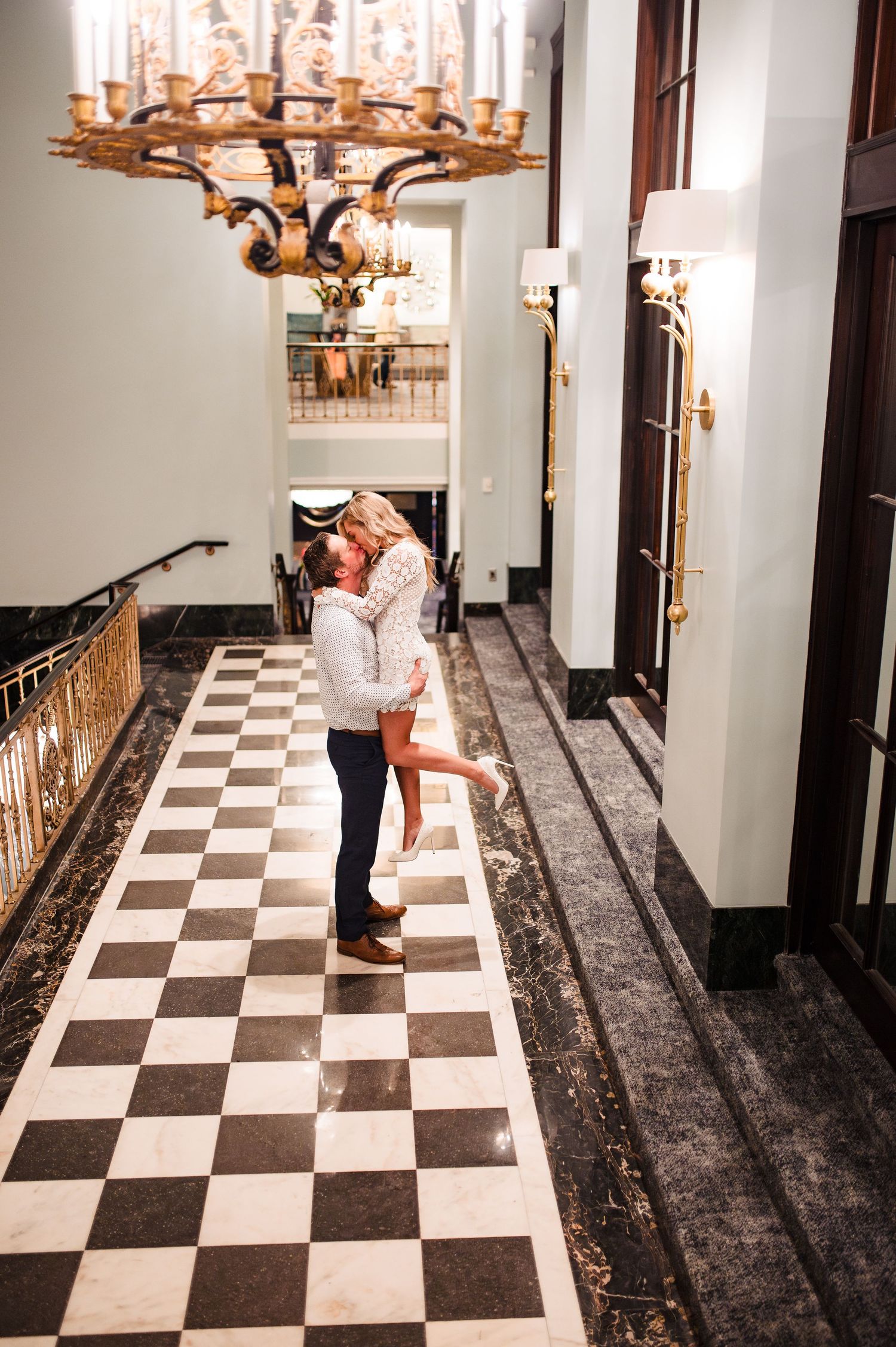 Elegant hallway with checkered floor and chandelier creates dramatic setting for couple.