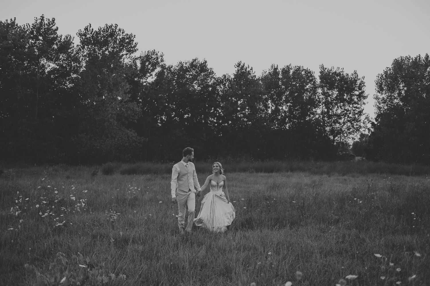 Black and white landscape photograph showing figures walking through a serene meadow at dusk.