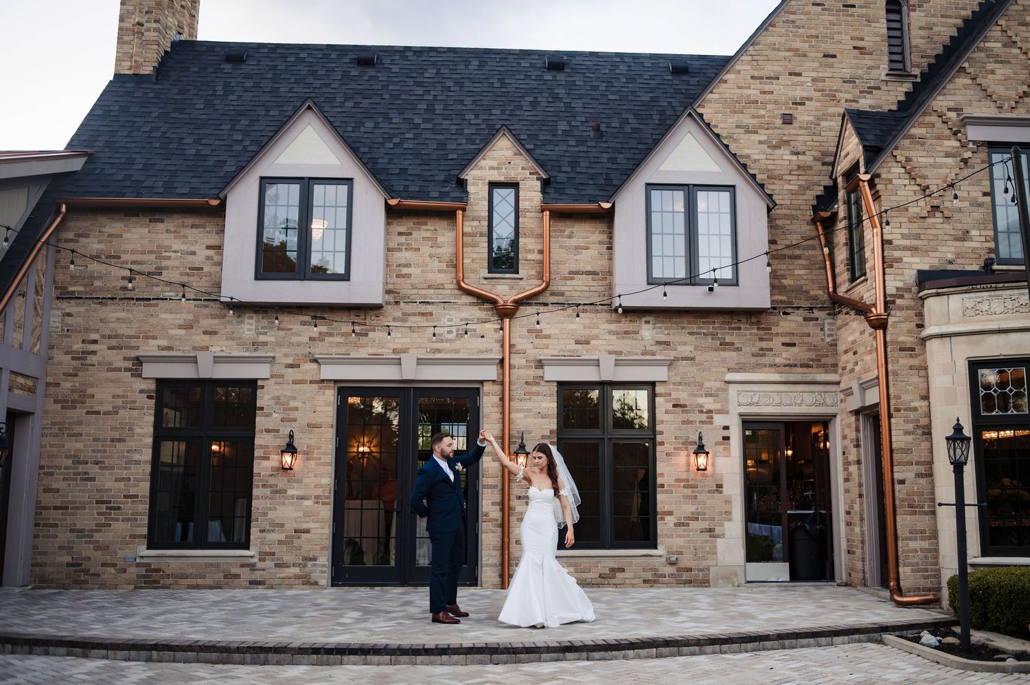 Wedding couple poses playfully outside stone building with dramatic lighting and architectural details.