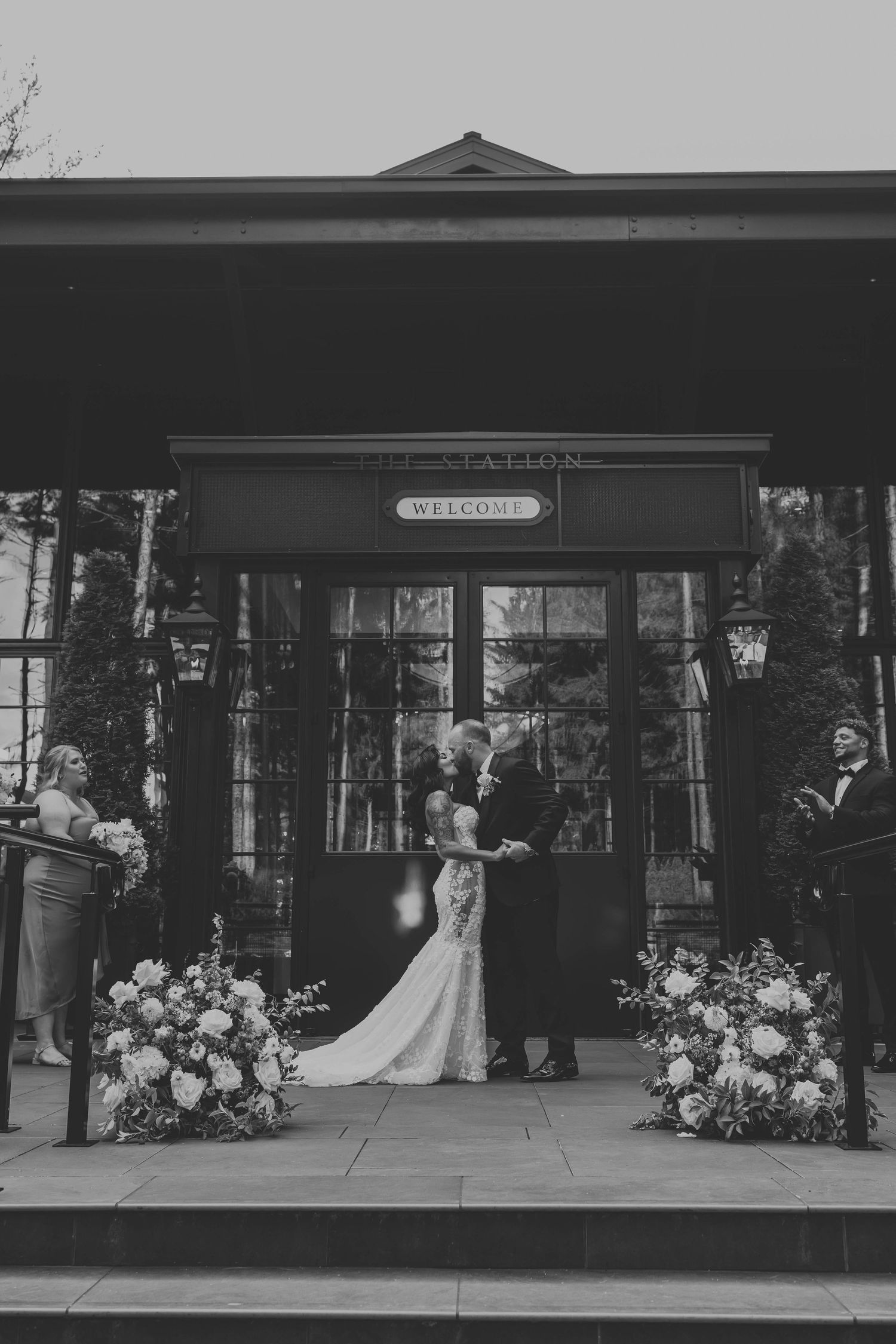 Black and white wedding photos outside a vintage train station with floral arrangements.
