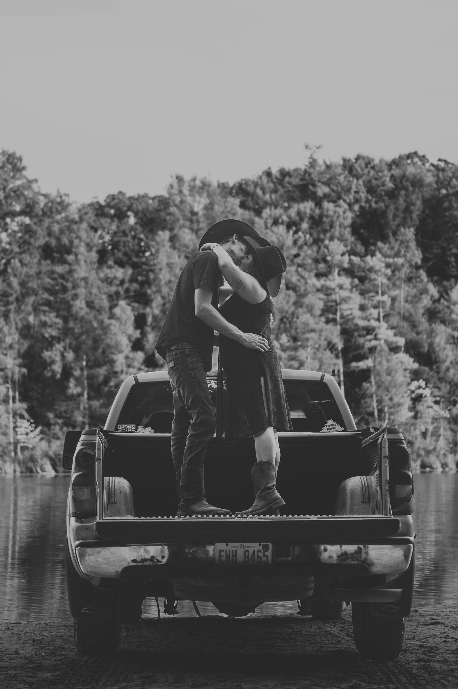 Couple sitting on pickup truck bed by scenic lake in black and white.