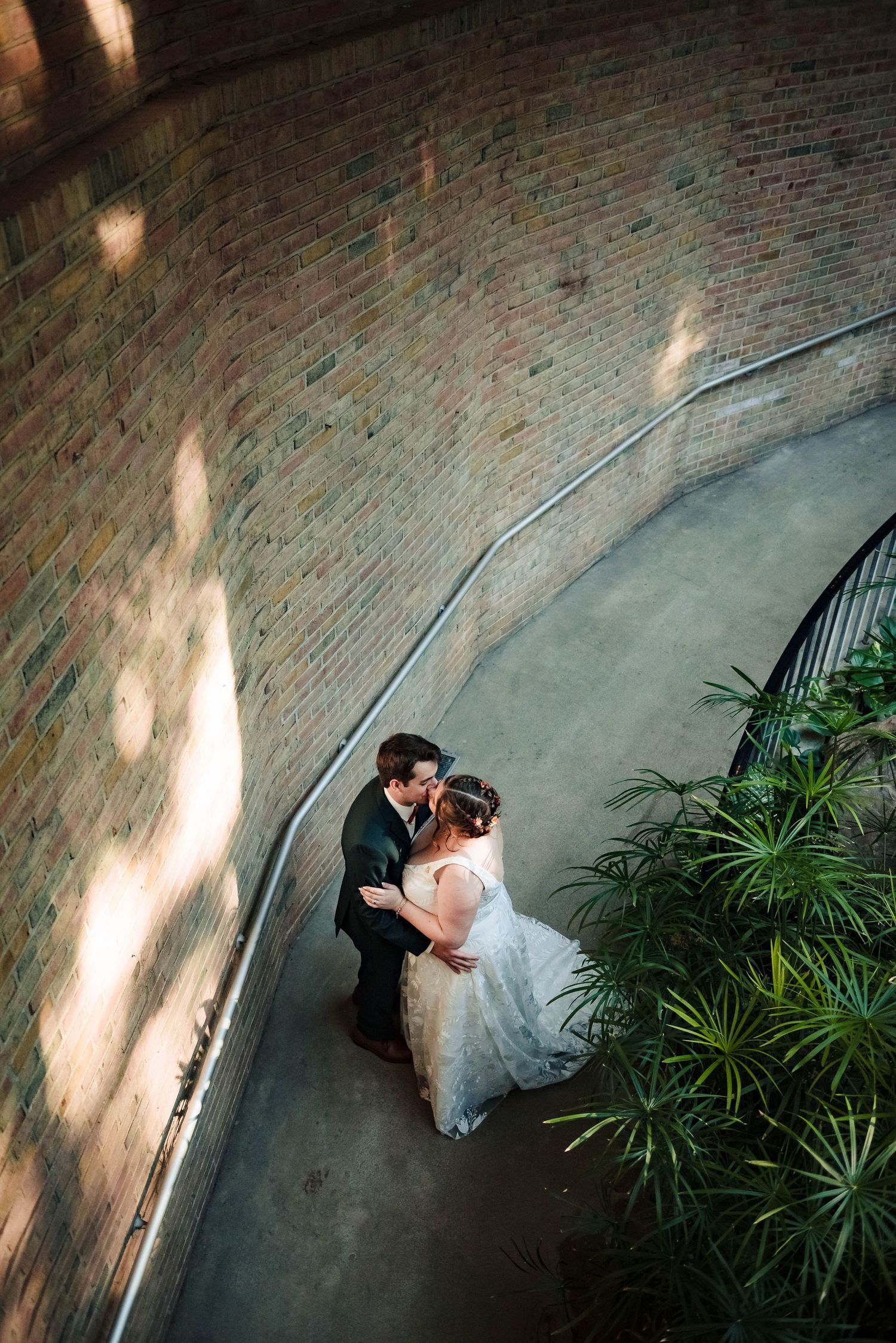 Aerial view of a couple dancing in an elegant venue with brick walls and potted plants.