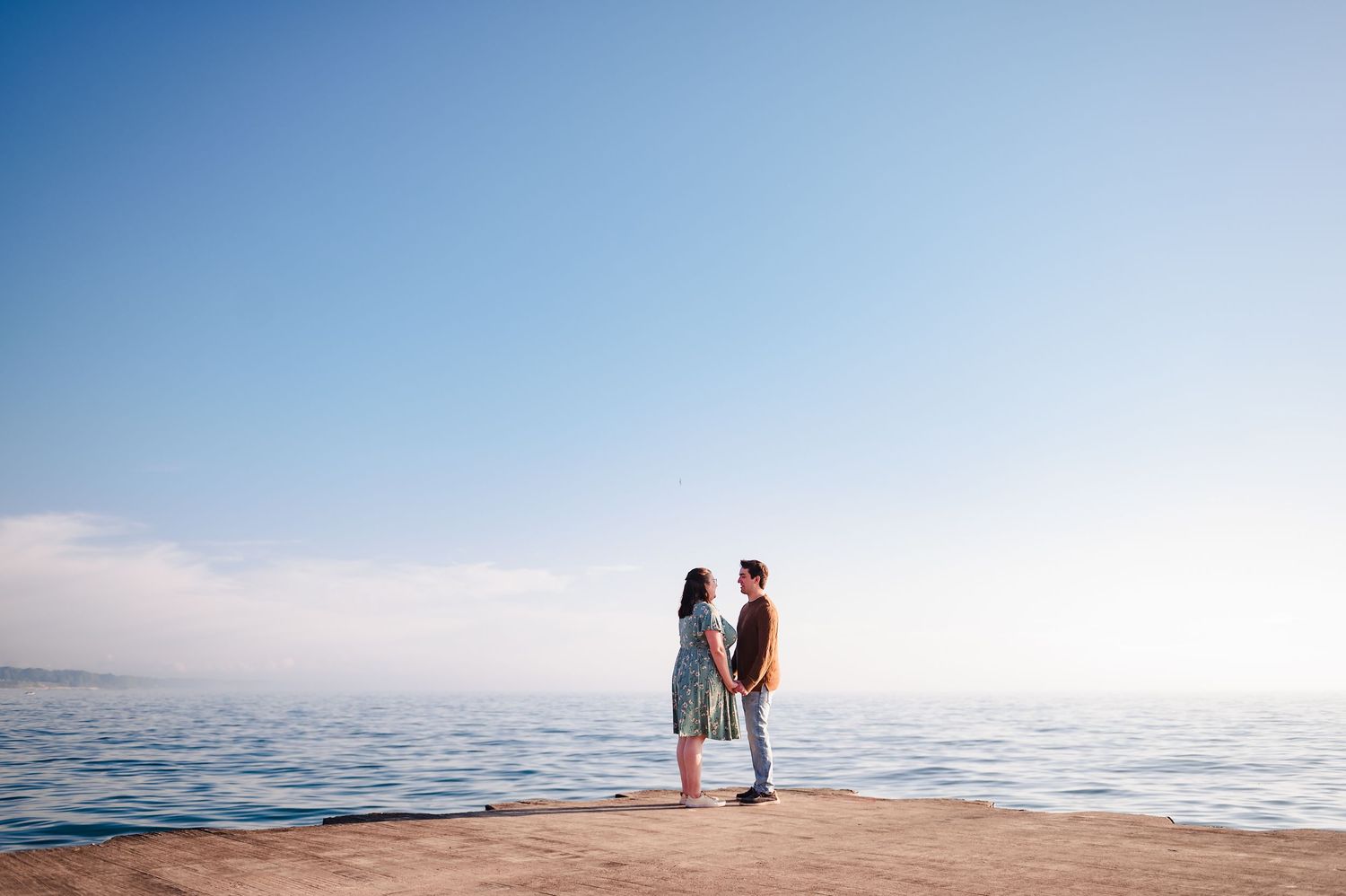 A couple stands together on a pier overlooking the ocean during a serene sunset moment.