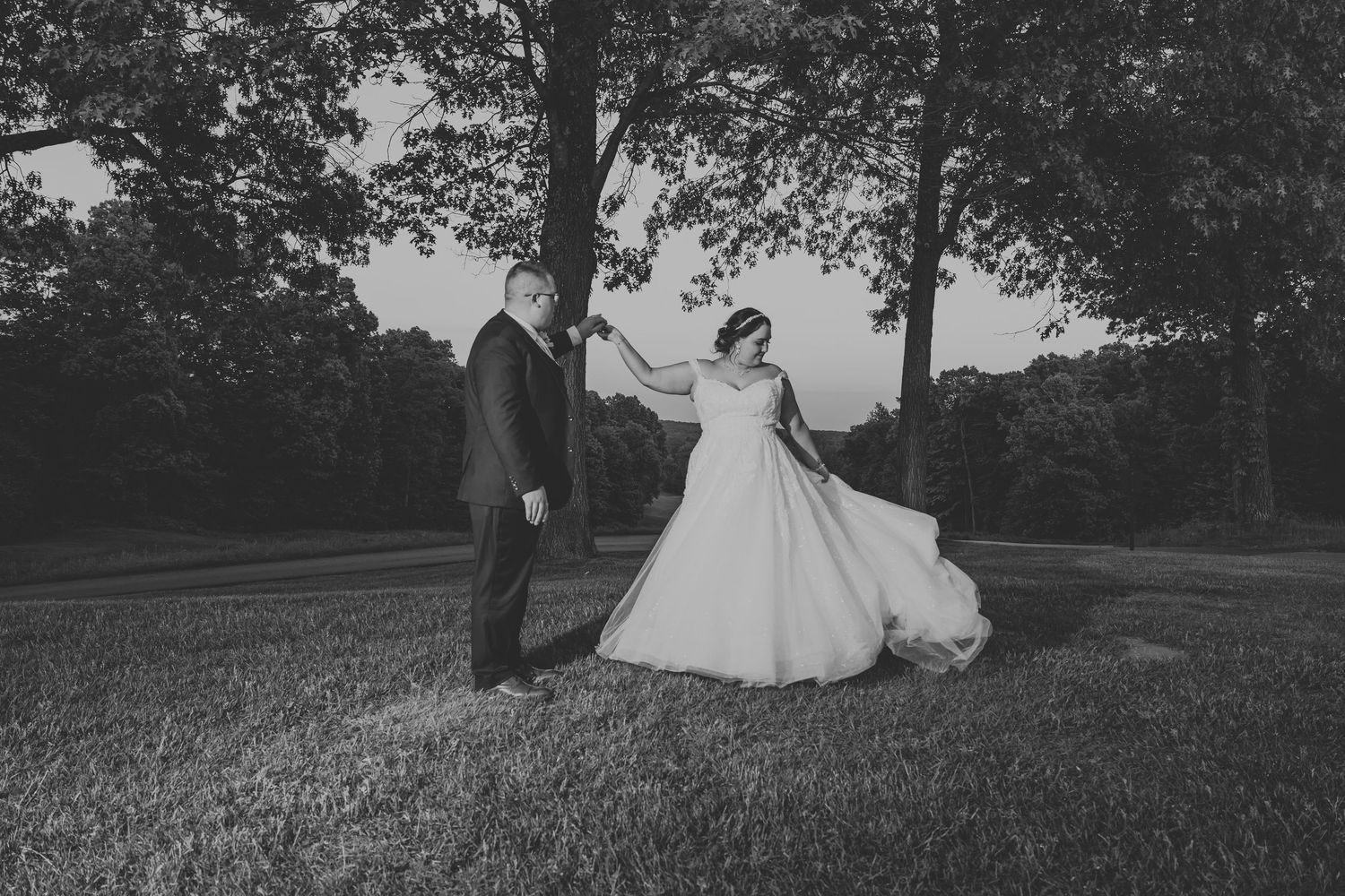 Romantic black and white photograph of a couple sitting together on a grassy hillside in vintage formal attire.